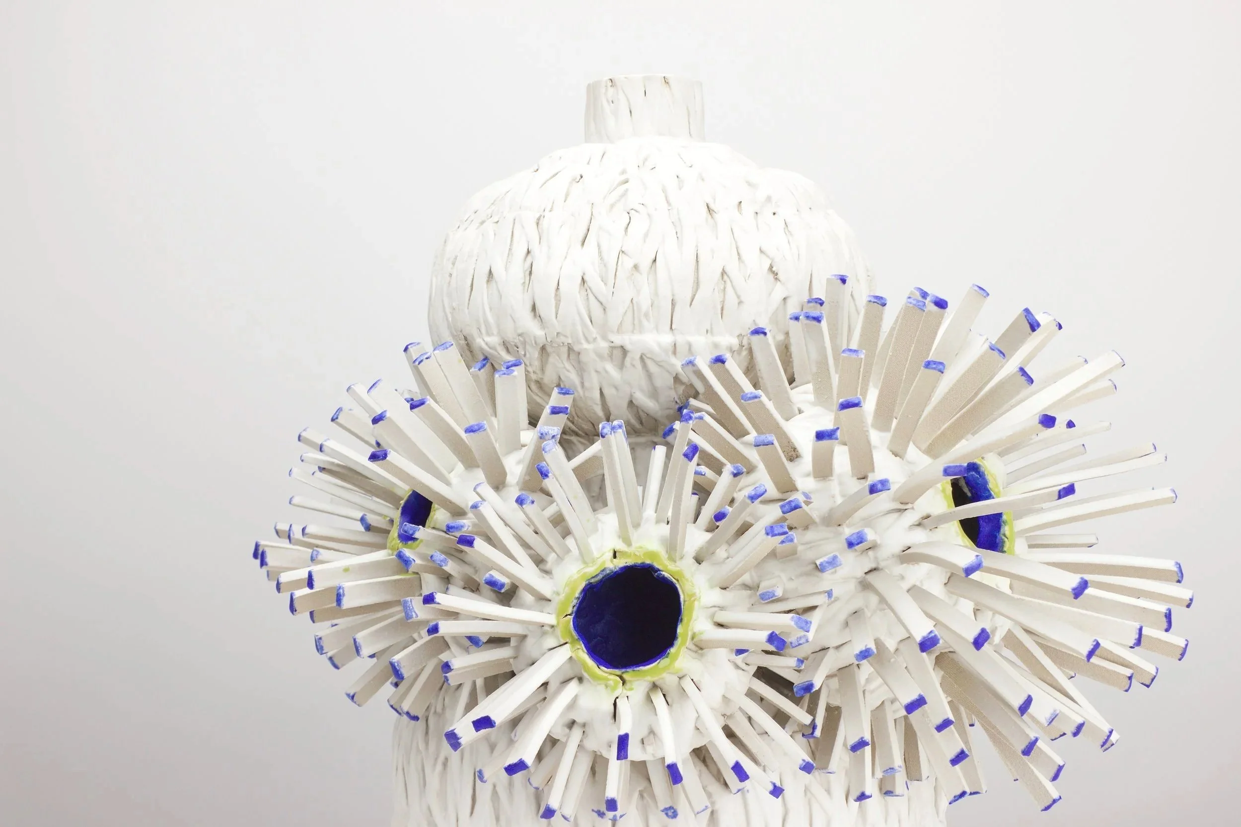 Ein kreatives Kunstwerk aus zusammengefügten weißen Foam-Sticks, mit blauen Enden, das eine weiße Vase und eine Vielzahl von Foam-Sticks um die Vase herum darstellt.