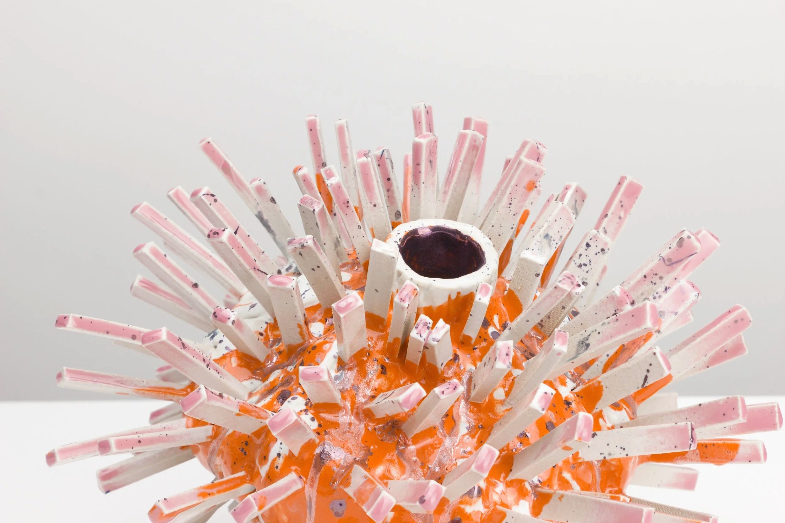 Kunstwerk aus orangefarbenen, weißen und pinkfarbenen Materialien mit schwarzen und orangefarbenen Sprenklern, das eine strukturierte, spiky Form hat.
