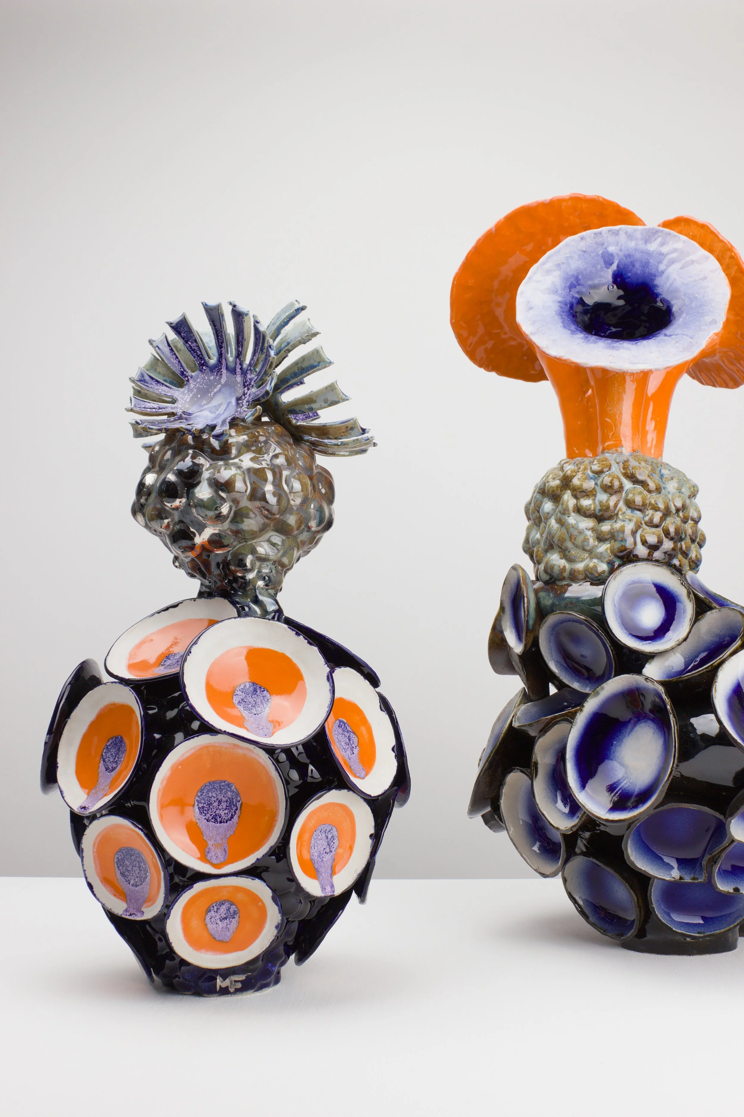 Keramikplastiken in Form von bunten Früchten mit Mustern in orange, blau, schwarz und weiß, auf weißem Hintergrund displayt.