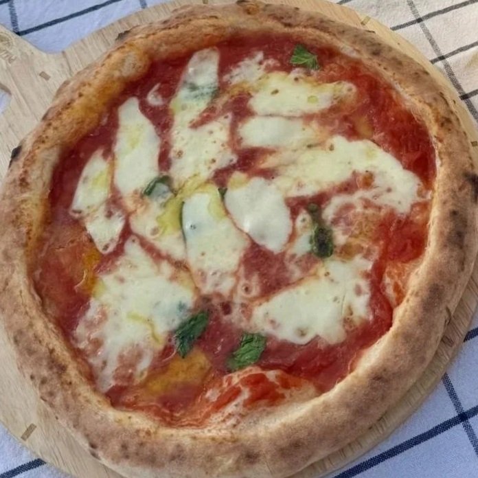 Pizza Margherita - mit Tomate, Käse und Basilikum auf einem Holzbrett.