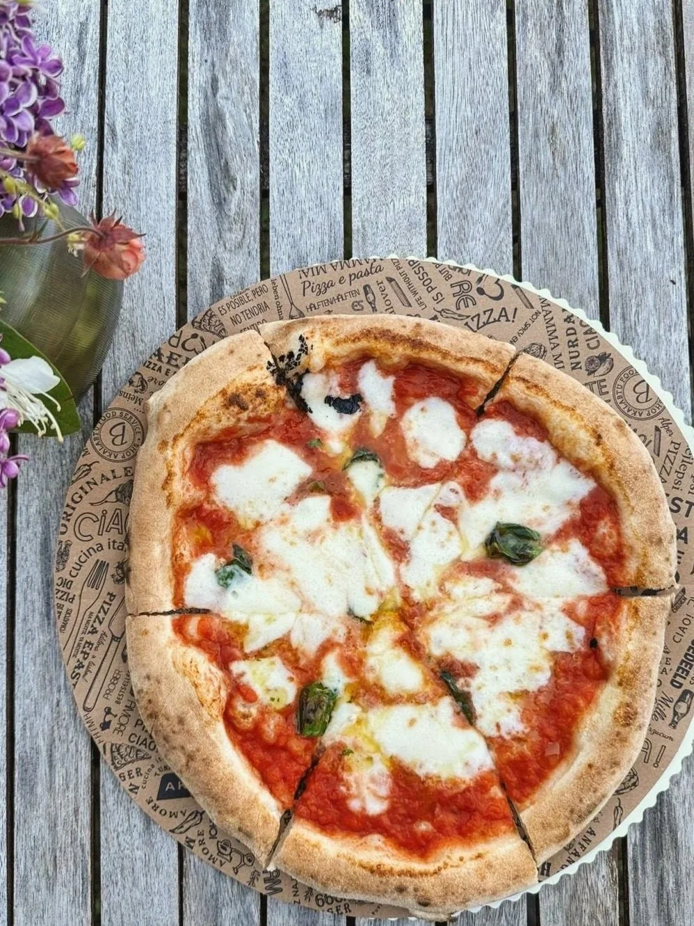 Eine Pizza mit Tomate, Mozzarella und Basilikum auf einem Holztisch.