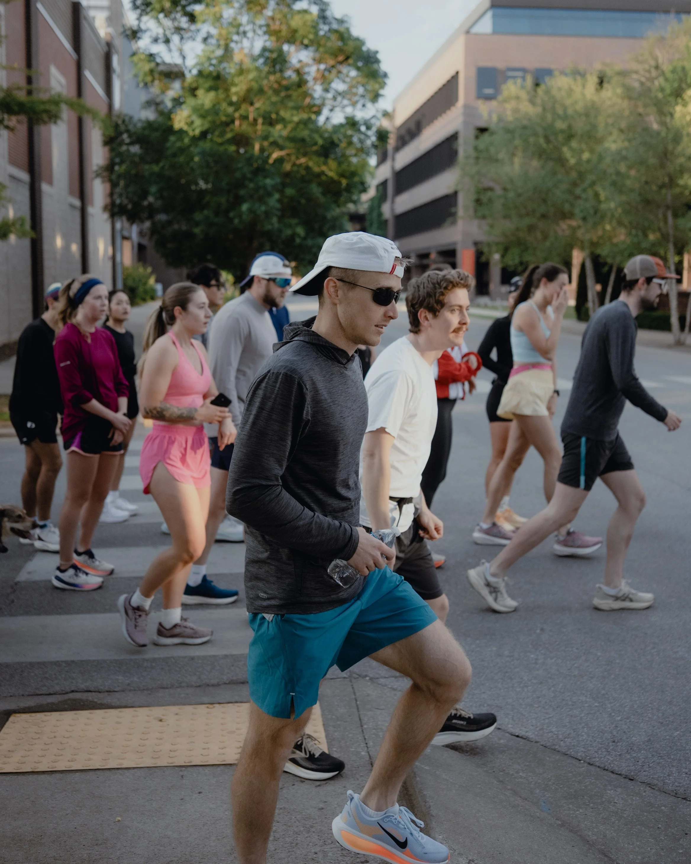 A group of people participating in an outdoor running event on a city street, dressed in athletic clothing with some wearing sunglasses and hats.