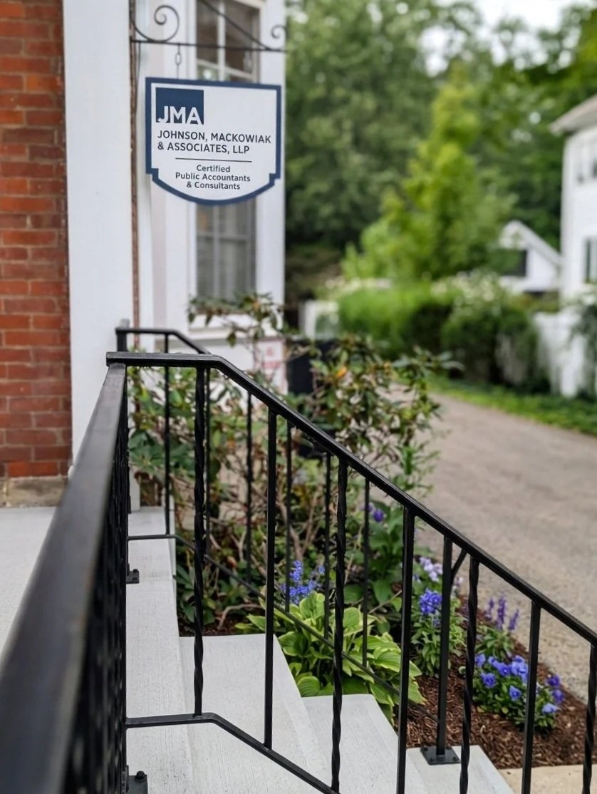 A house with a brick wall and a white door displaying a sign for Johnson, Mackowiak & Associates, LLP, certified public accountants & consultants. Johnson, Mackowiak & Associates, LLP (JMA) is a Western New York premier accounting and CPA firm.