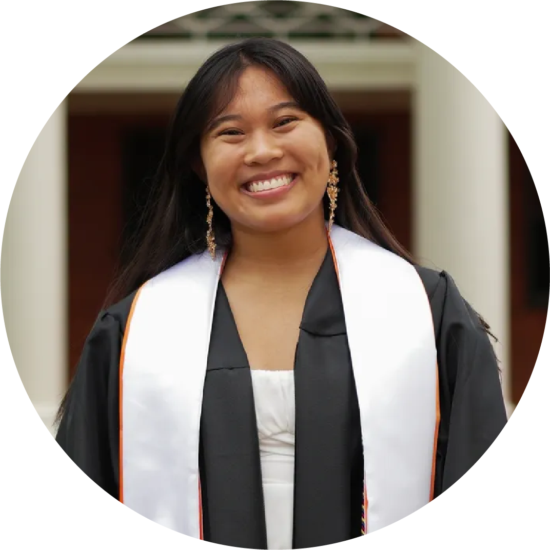 Young woman, Cheryll Caalim, wearing graduation gown and stole, smiling outdoors.