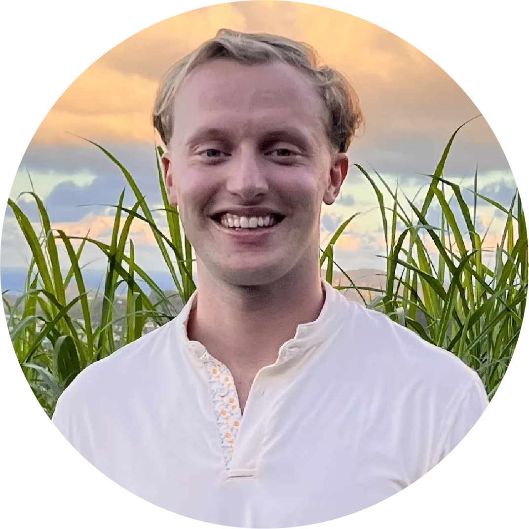 Young man, Bradley Rotondi, smiling outdoors with tall grass and a sunset sky in the background.