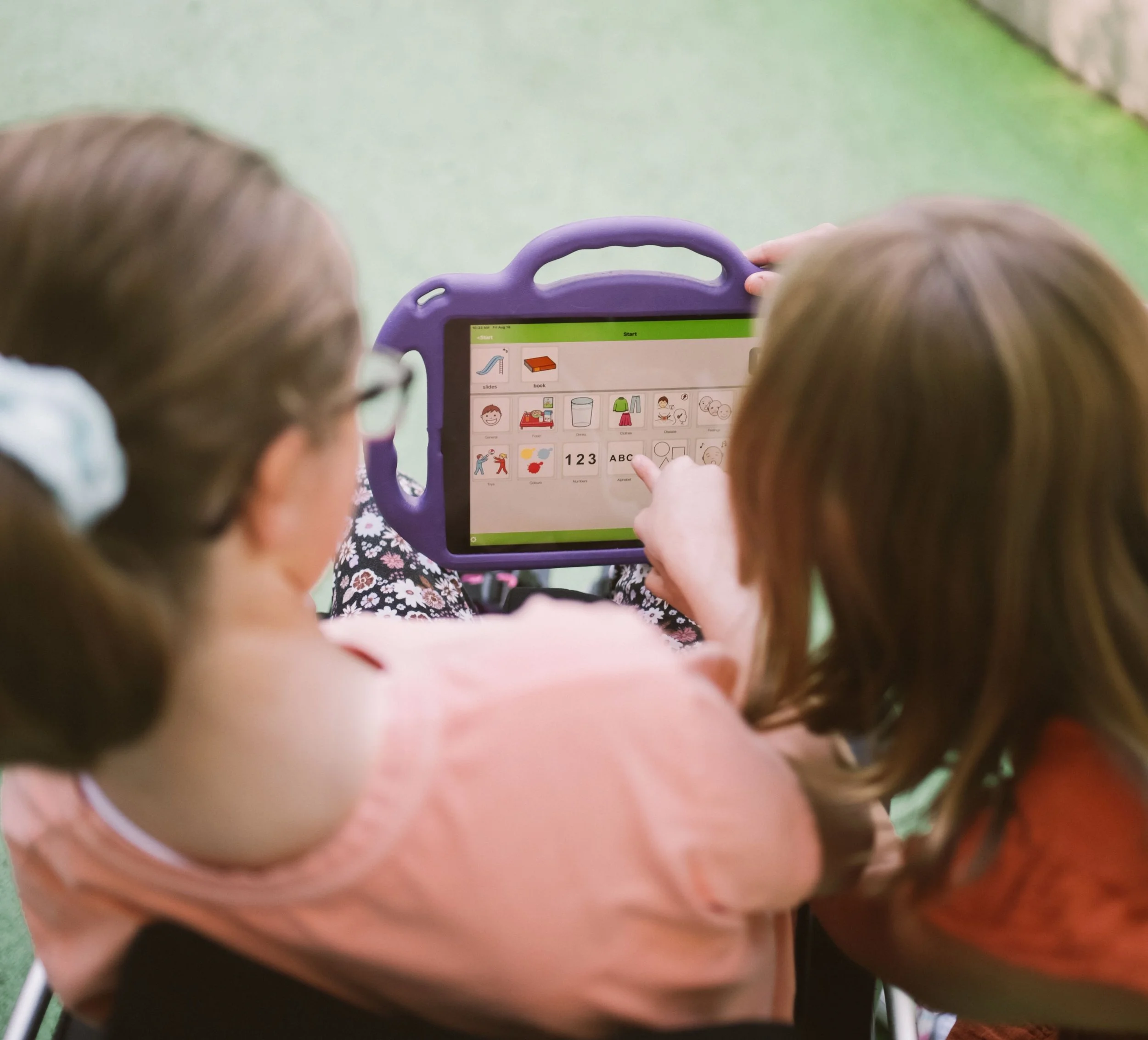 Children using a tablet with a purple protective case, with icons of slides, books, and children displayed on the screen.
