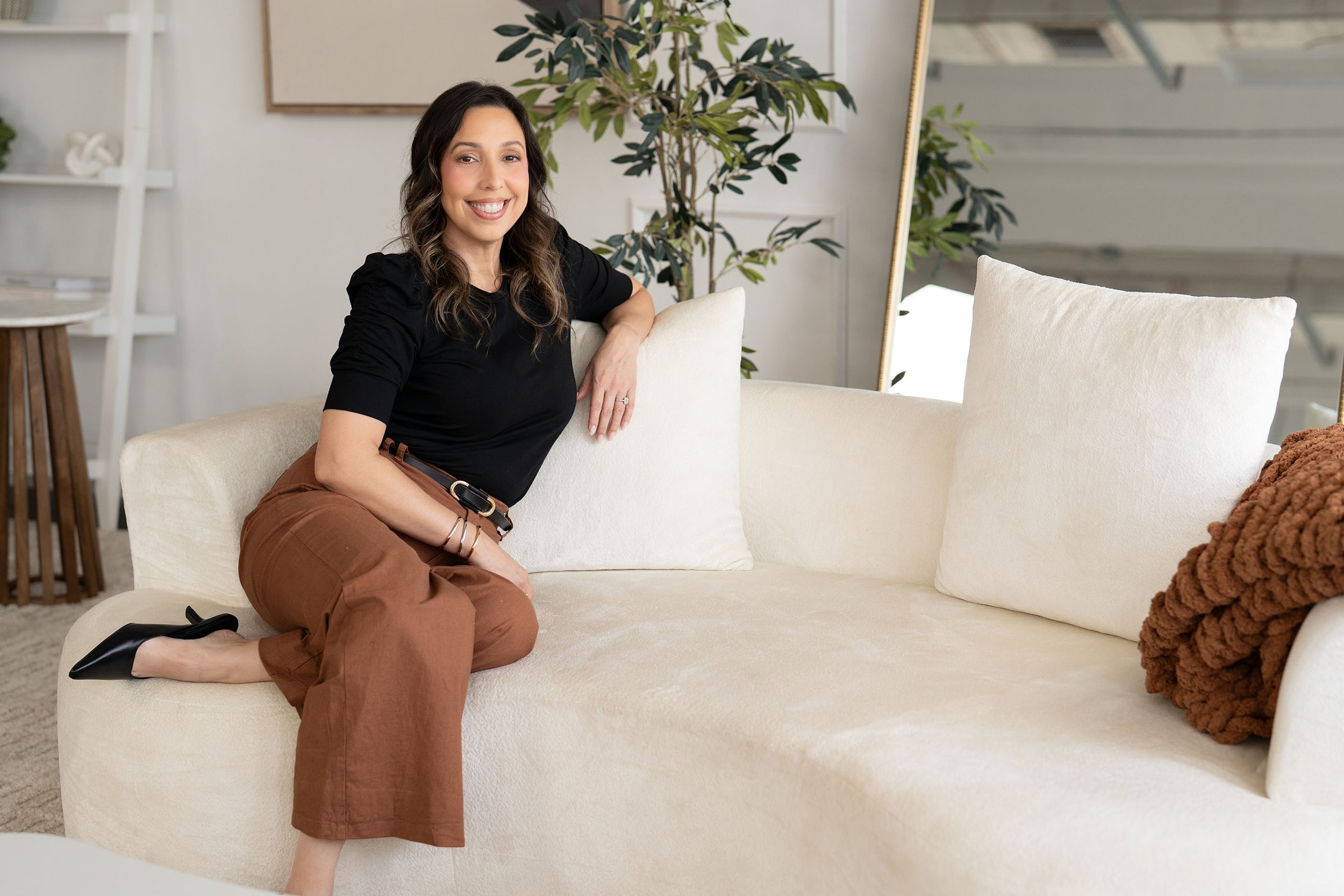 Leslie Gil, LMHC, smiling while seated on a sofa in a bright office.