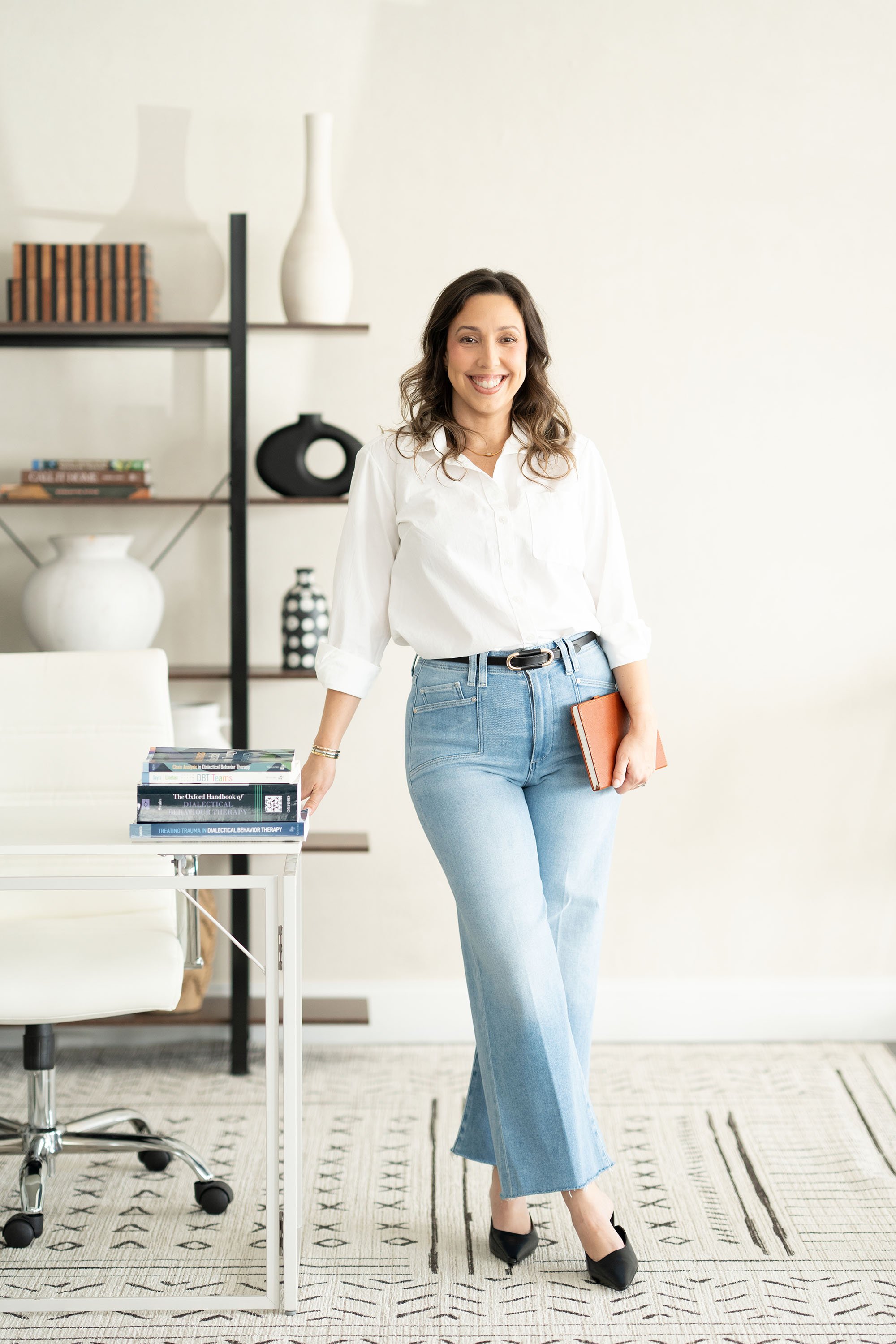 Leslie Gil, LMHC, standing beside a bookshelf in a bright office.