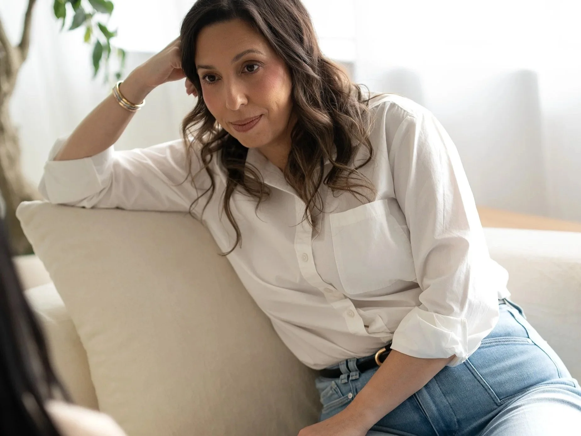 Leslie Gil, LMHC, sitting thoughtfully on a sofa at The DBT Collective, where she provides therapy for emotional regulation and intense emotions.