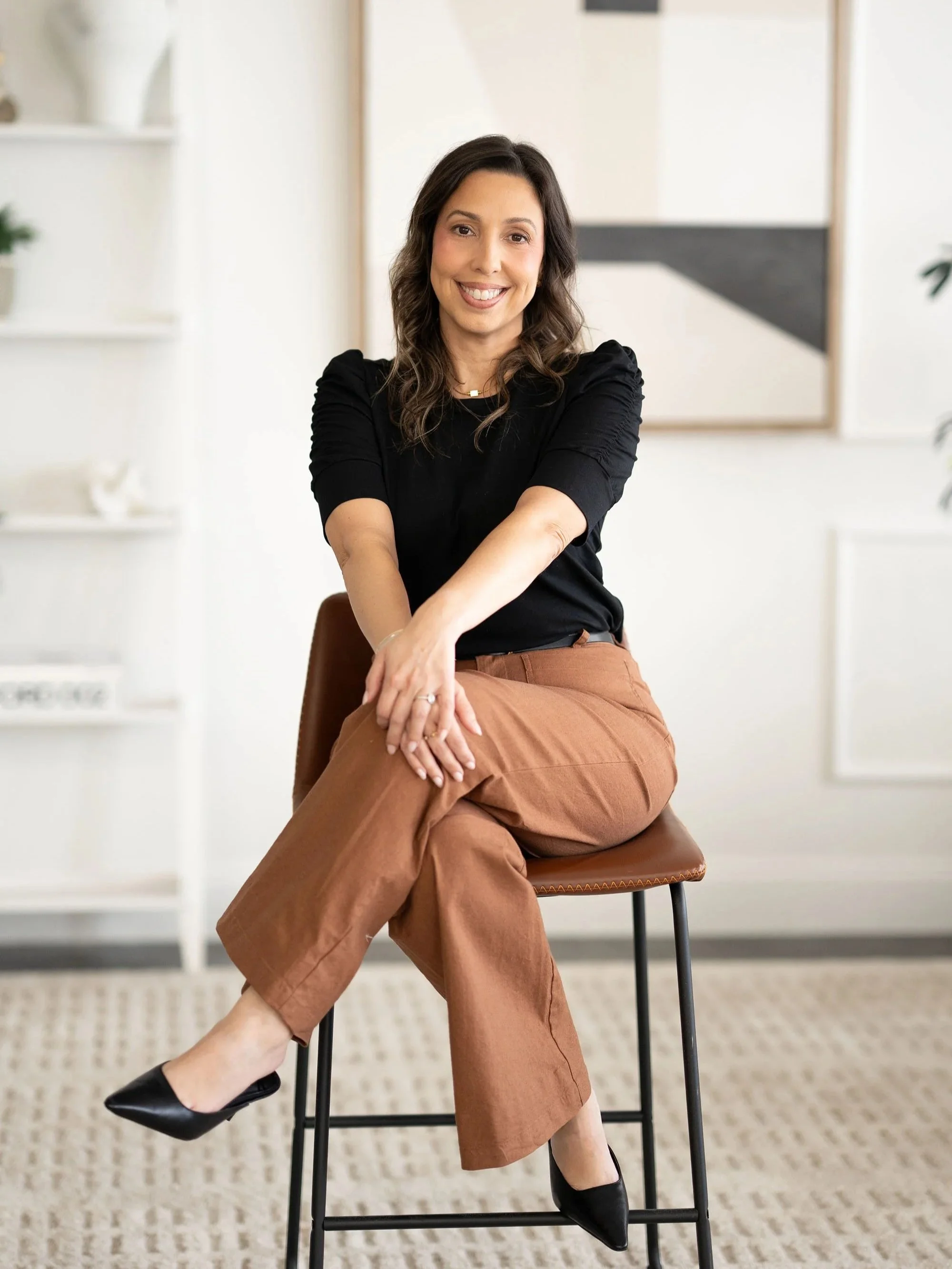 Leslie Gil, LMHC, seated in a chair and smiling in a bright office.