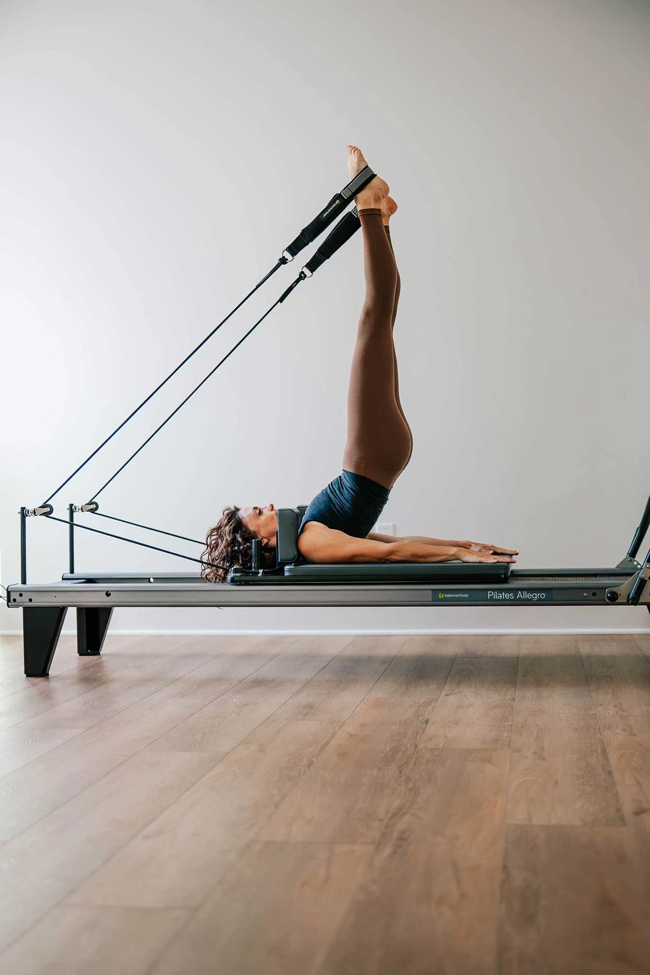 Pilates instructor Kim Russell demonstrating a move with her legs in the air on a reformer