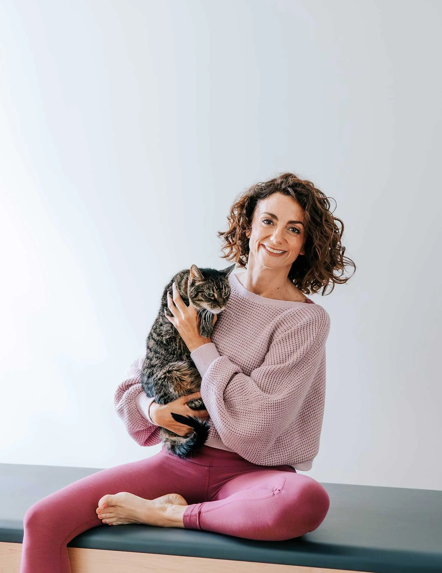 Pilates instructor Kim Russell sitting on a reformer with a cat