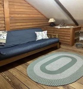 Living room corner with a blue sofa, wooden side table, lamp, and an oval patterned rug on wooden floor