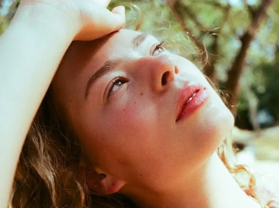 A young woman with curly hair resting outdoors, gazing upward with a relaxed expression.