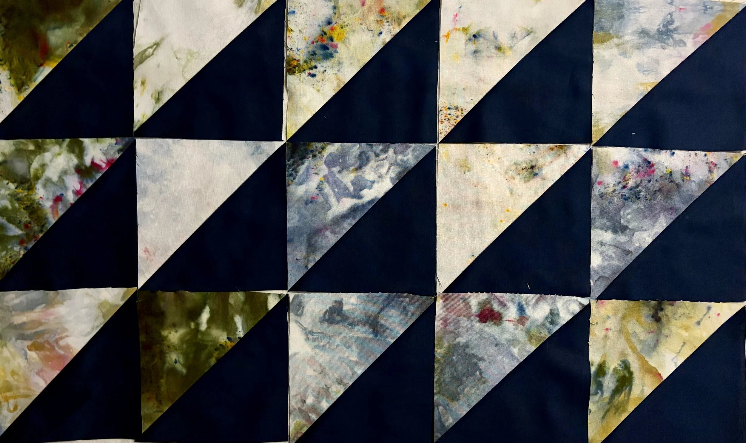 A quilt with a pattern of black triangles and fabric squares with multicolored abstract splashes and patterns.