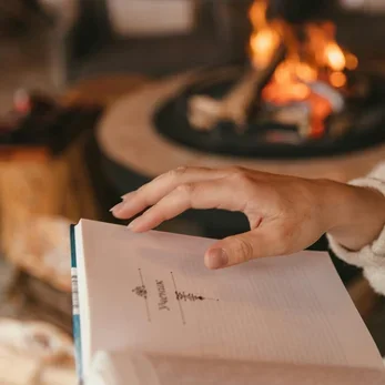 Person opening a notebook in front of a lit fireplace
