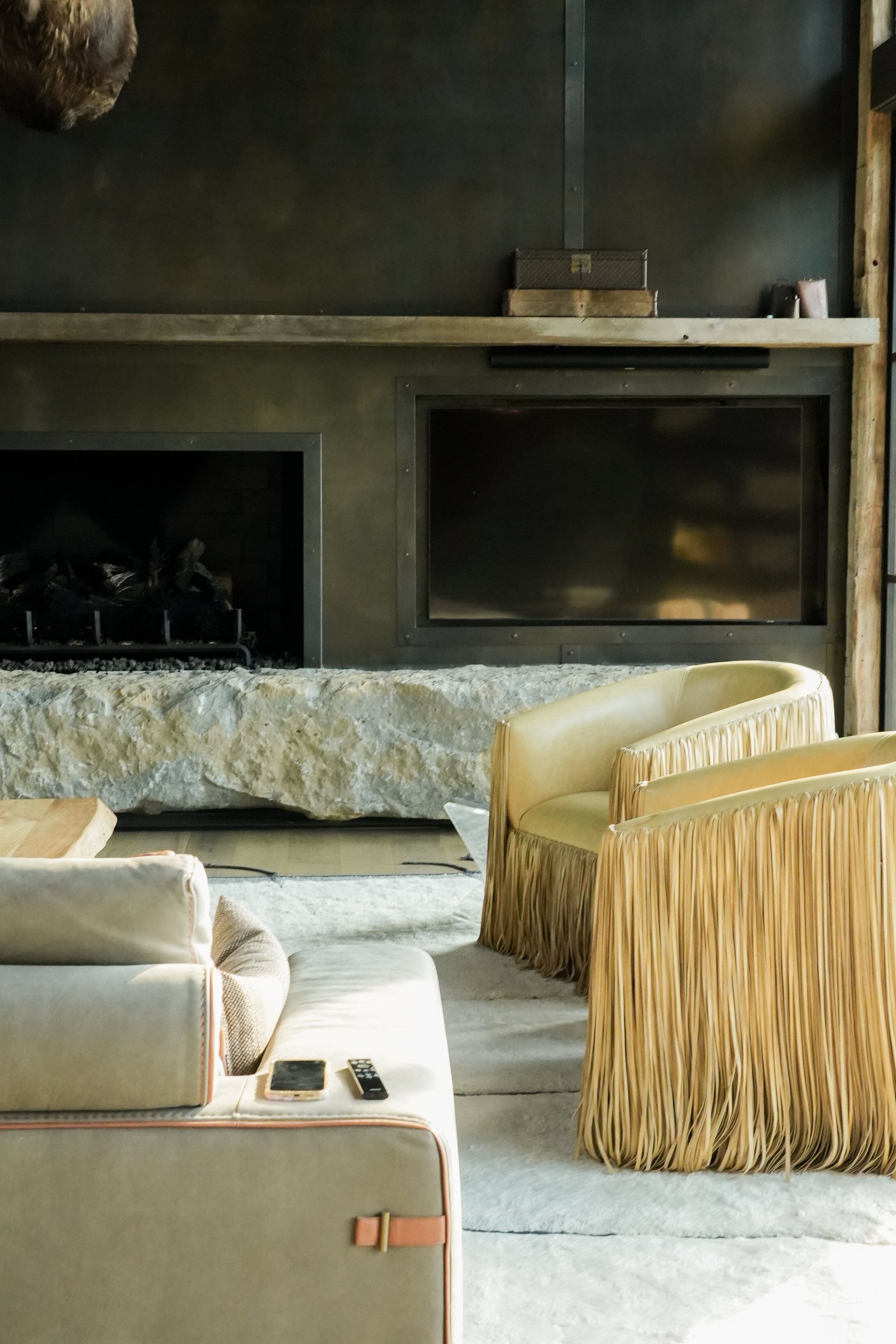 Living room with a beige sofa with tassels, a TV, a stone fireplace, and a black TV in the background.
