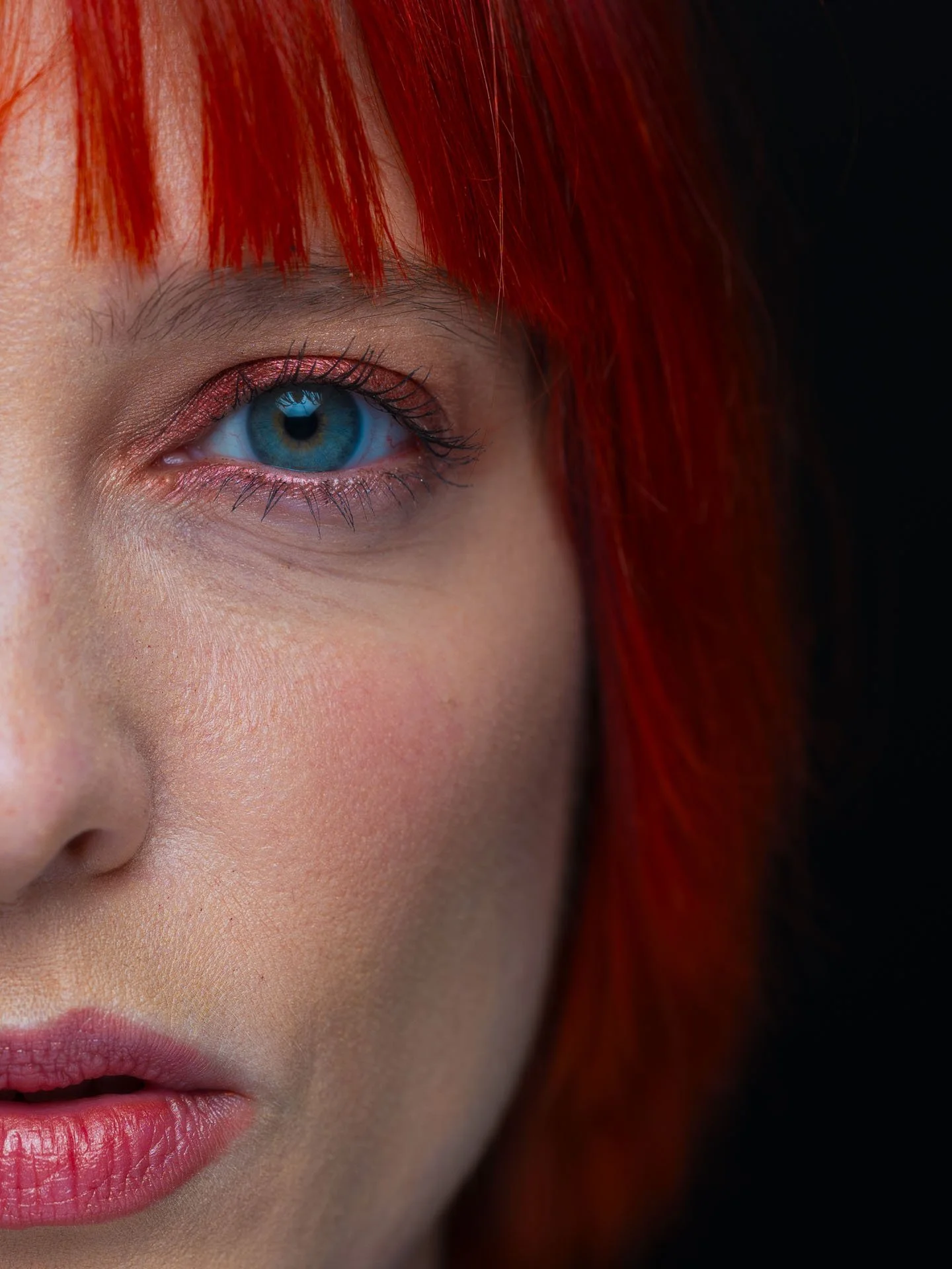 Dichter bij gezicht met blauw oog, rood haar, lichte huid, en roze lippen.