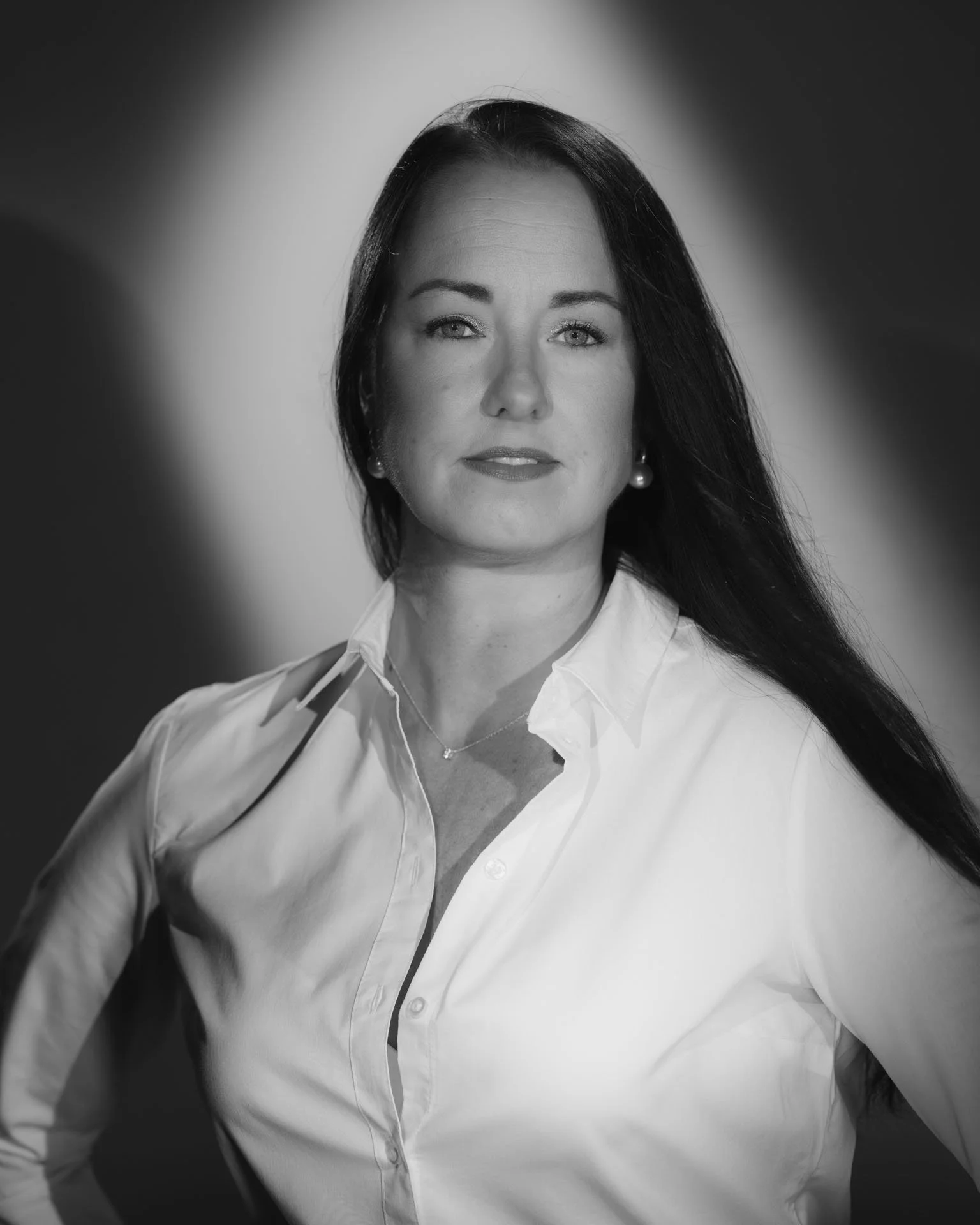 Zwarte en witte portretfoto van een vrouw met lang zwart haar, witte blouse en parel oorbellen, in zwart-wit.