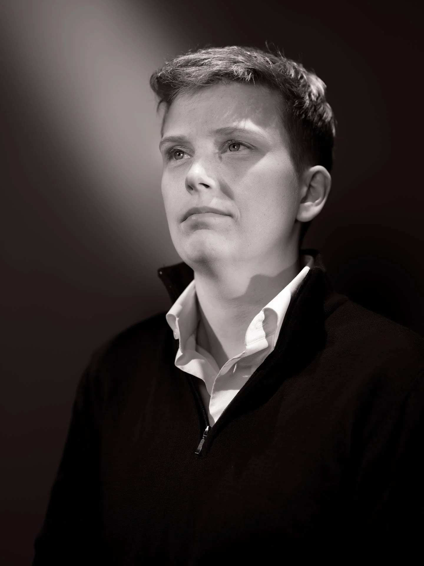 Zwart-wit foto van een man die naar links kijkt, met korte haren en een witte shirt onder een zwart jasje met een halve rits.