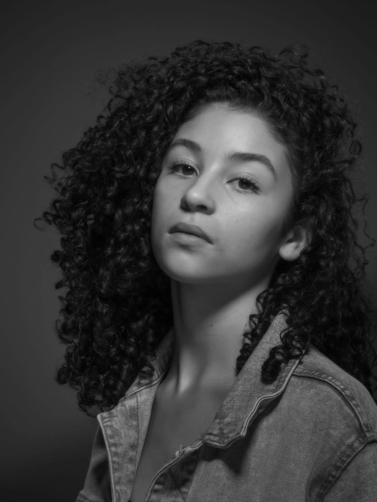 Zwart-wit foto van een jonge vrouw met krullend haar, gekleed in een denim jas.