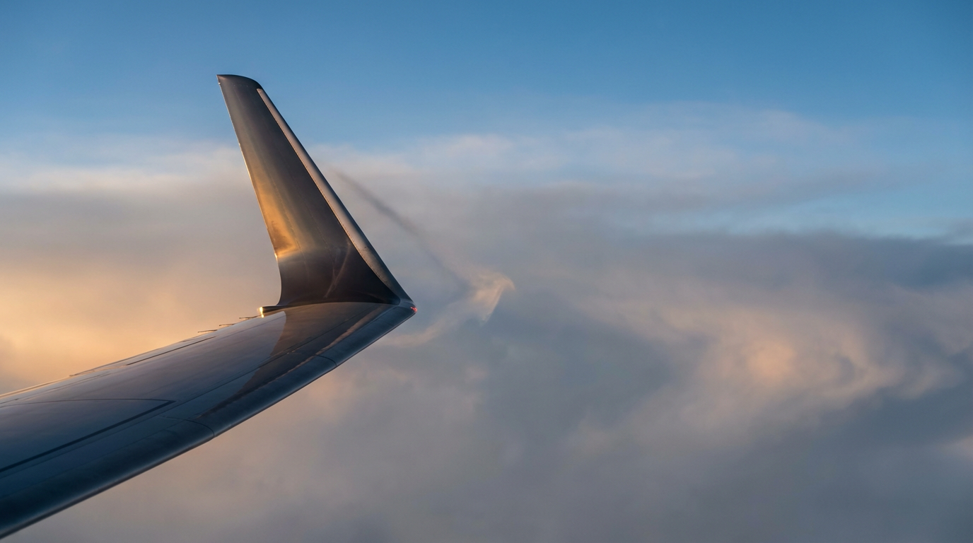 Close-up of an airplane's wingtip flying through the sky with clouds behind it.