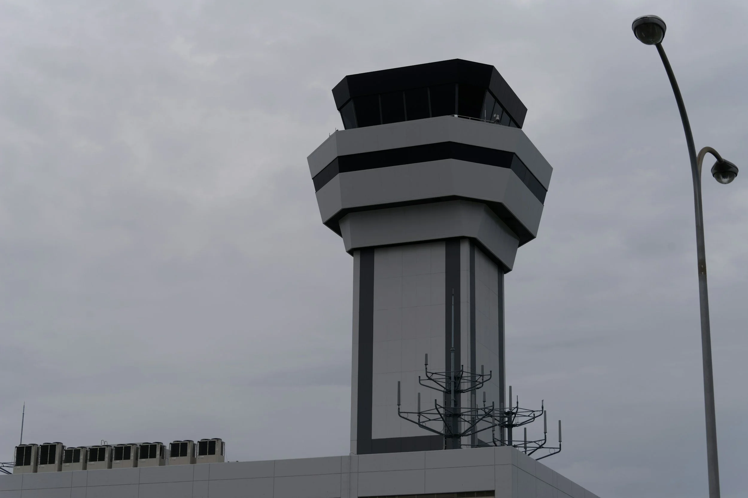 Image of an airport air traffic control tower under a cloudy sky.