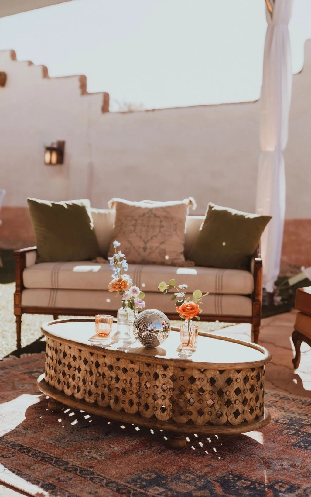 Bohemian living room with a vintage sofa, patterned coffee table, flowers, and mirrored decor in warm sunlight