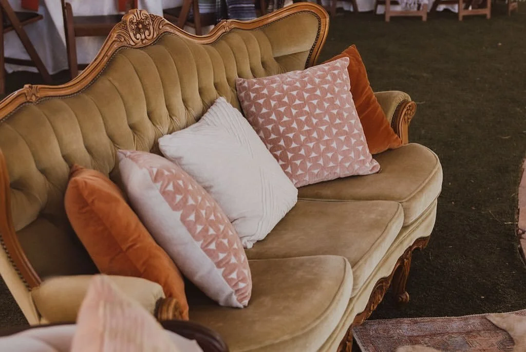 Vintage gold tufted velvet sofa with carved wood details and pink, white, and burnt orange pillows