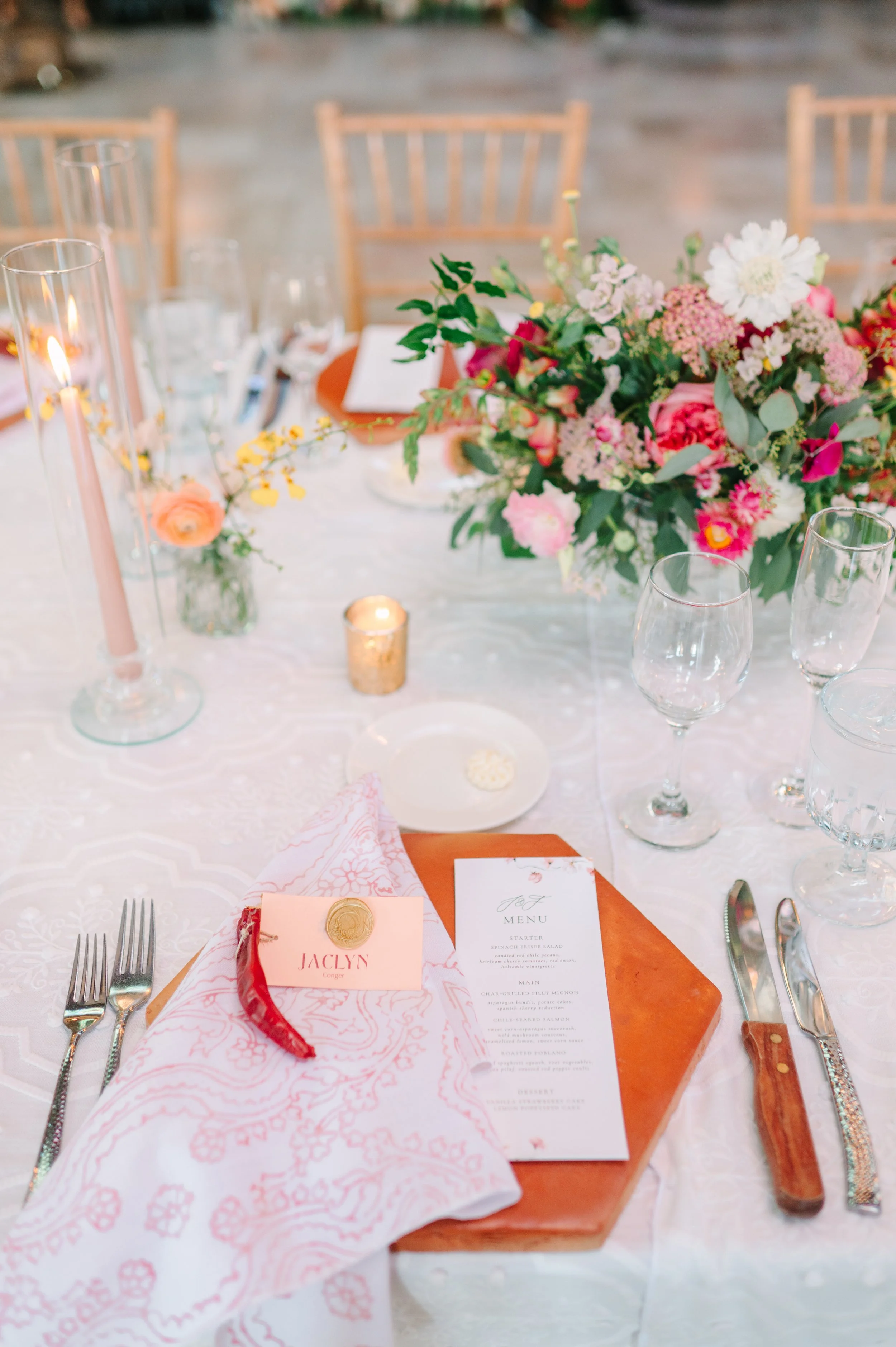 Elegant wedding reception table with colorful floral centerpiece, candles, place settings, menus, and wine glasses