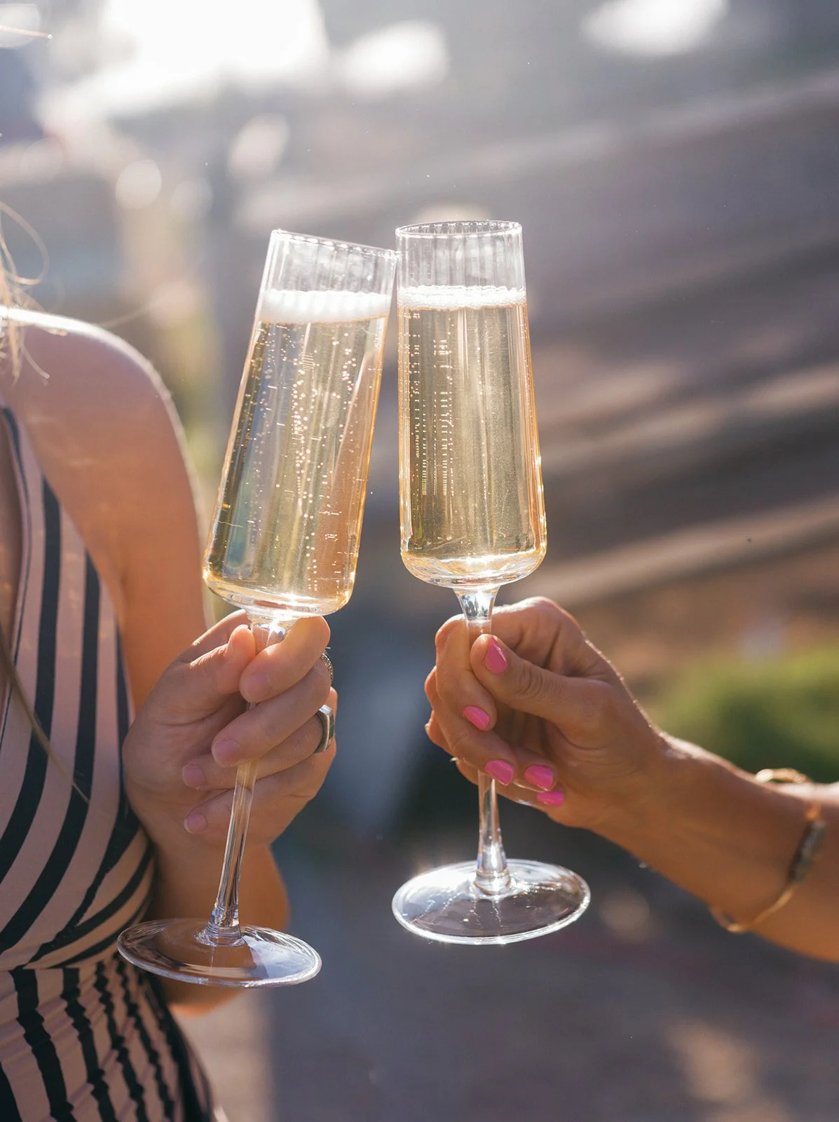 Two women clinking glasses of champagne outdoors during sunset.