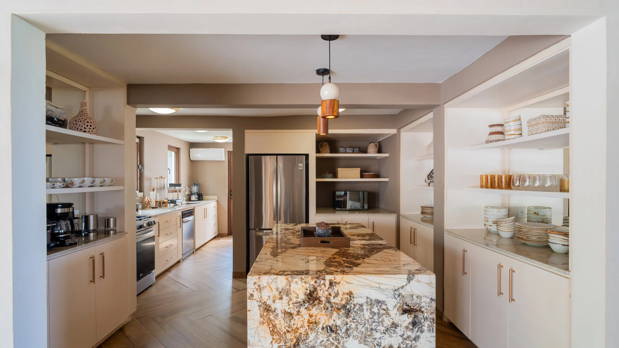 Modern kitchen with beige cabinets, open shelves with dishes, a marble island, and stainless steel appliances.