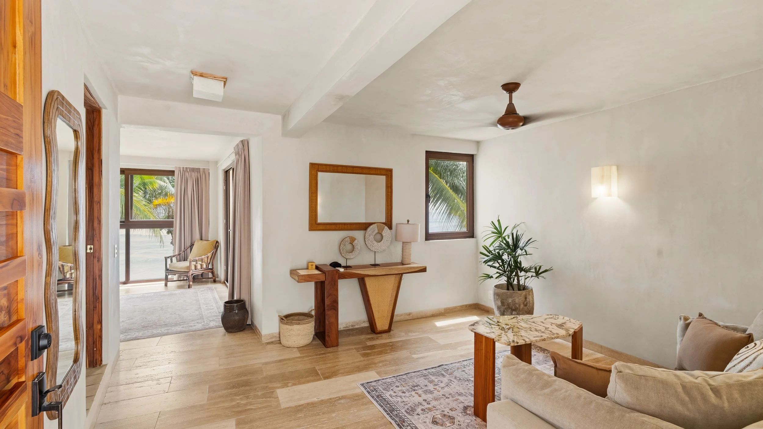 Living room with white walls, wooden furniture, a mirror, potted plant, large window, and ceiling fan.