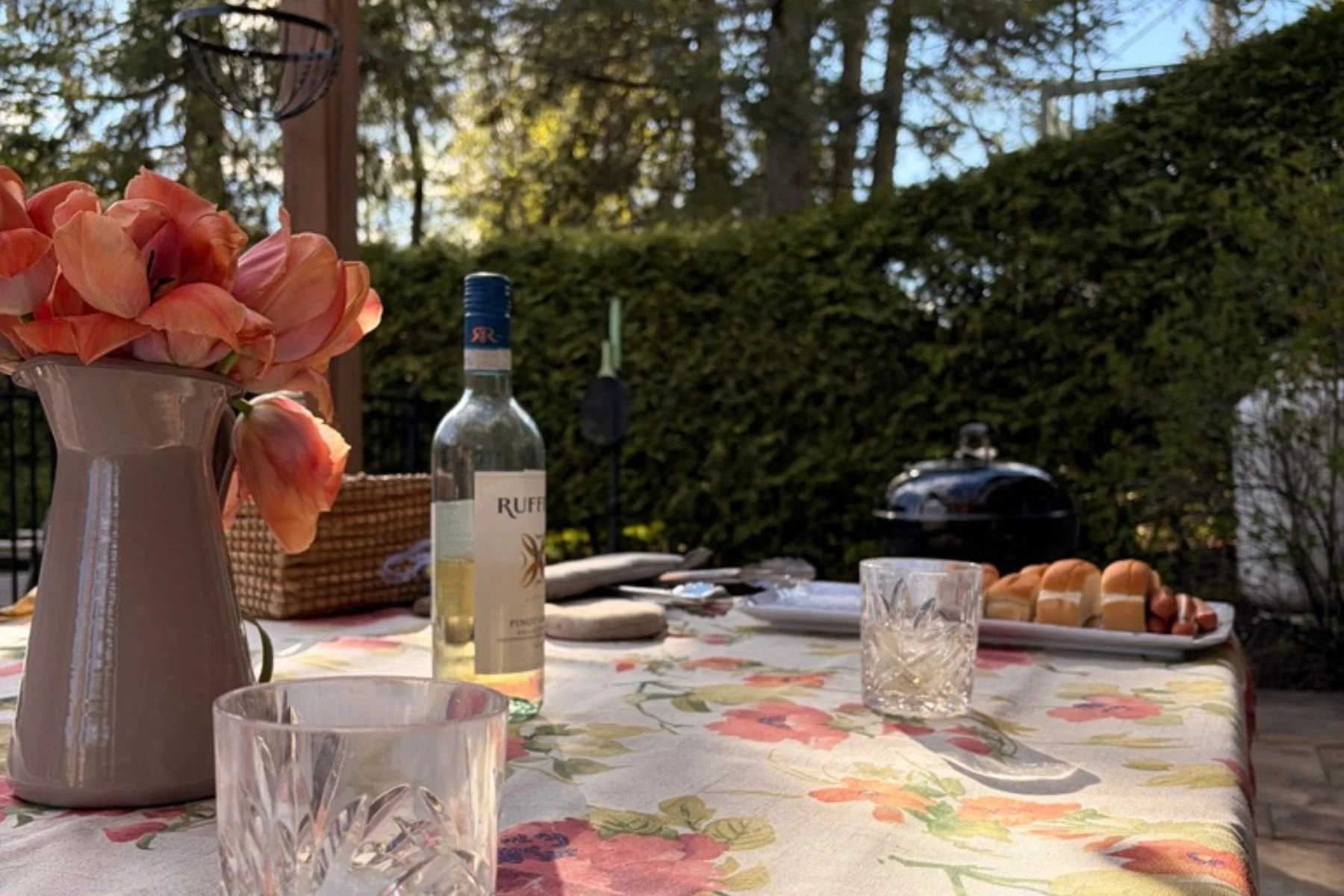 Outdoor table set with flowers, wine and food for a relaxed backyard gathering.
