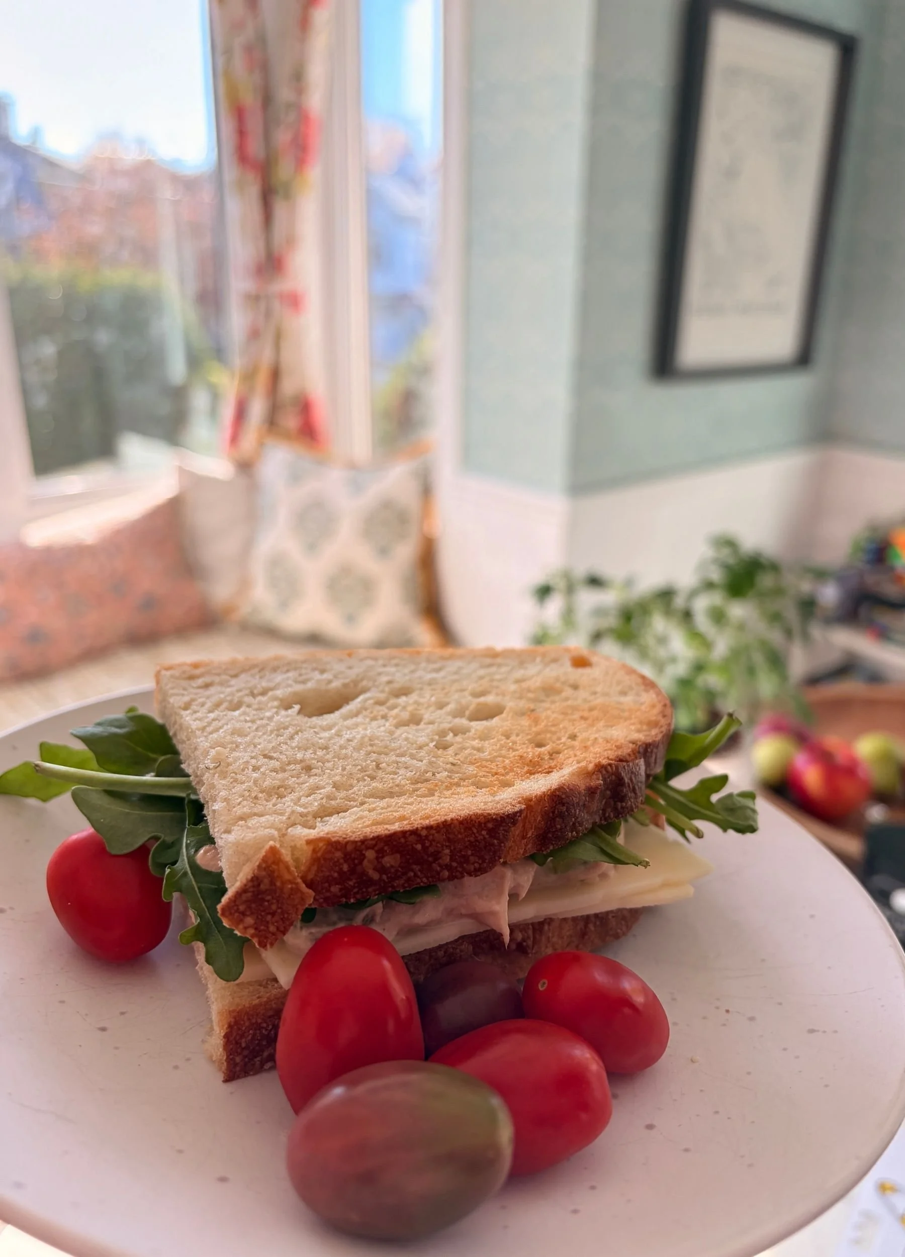 Toasted sourdough tuna salad sandwich layered with arugula and Swiss cheese, served on a plate with red cherry tomatoes.