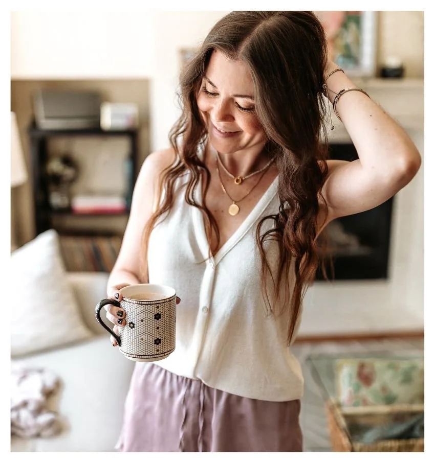 Woman at home holding a coffee mug in a bright, cozy living room.