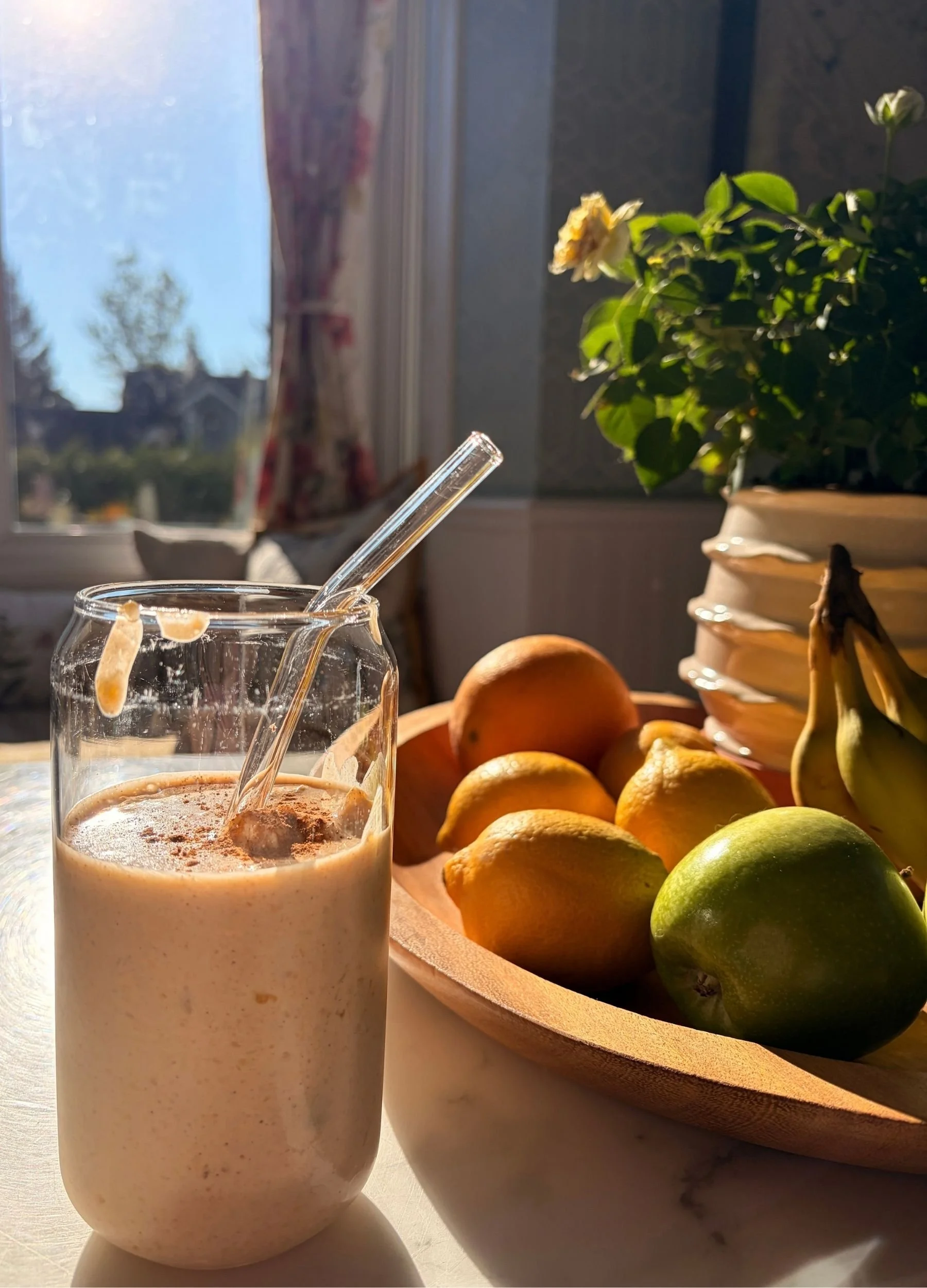 Creamy peach protein smoothie with cinnamon in morning sunlight beside a bowl of fresh fruit.