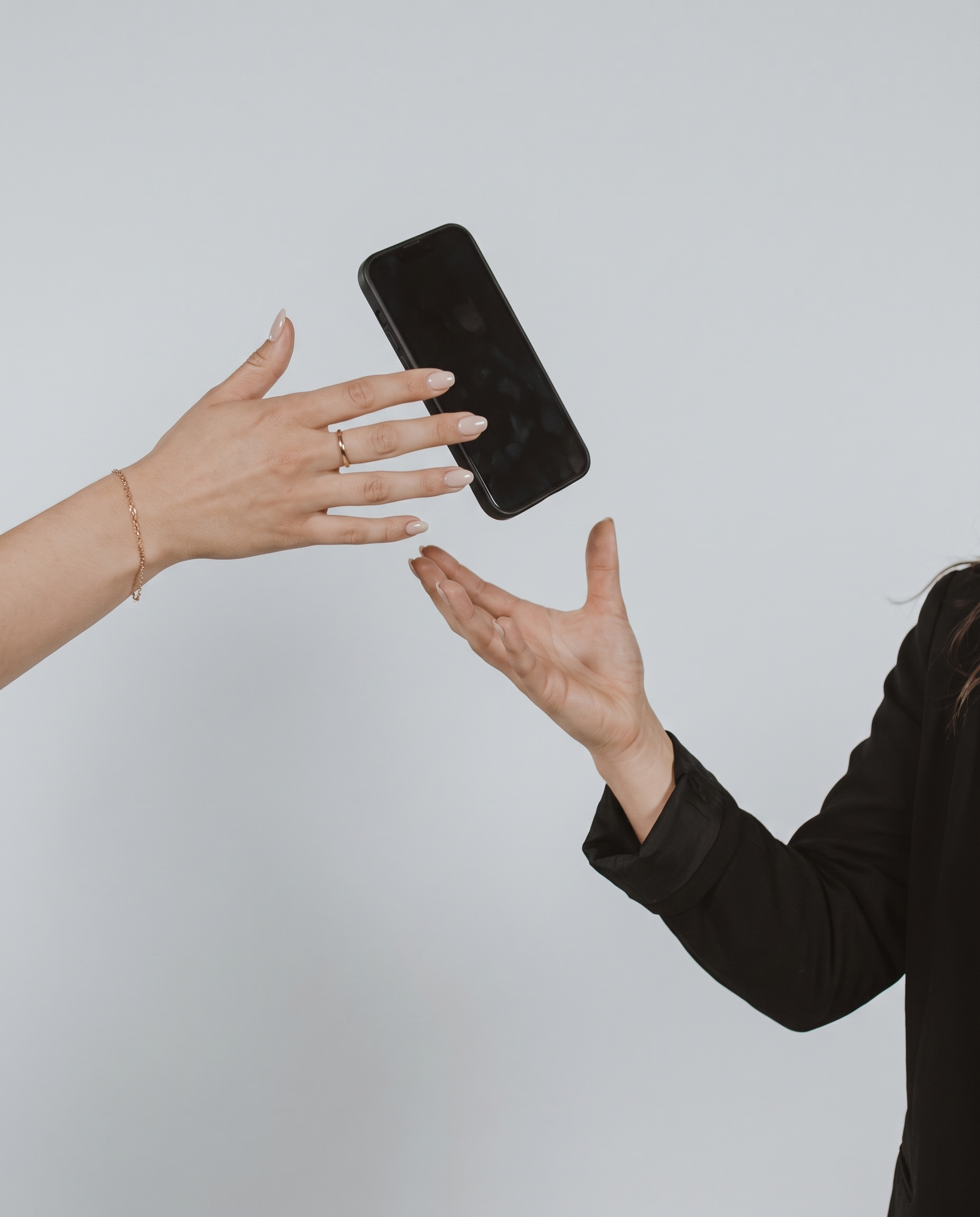 Close-up of a person's hand with manicured nails and a bracelet, holding a black smartphone against a plain light gray background.