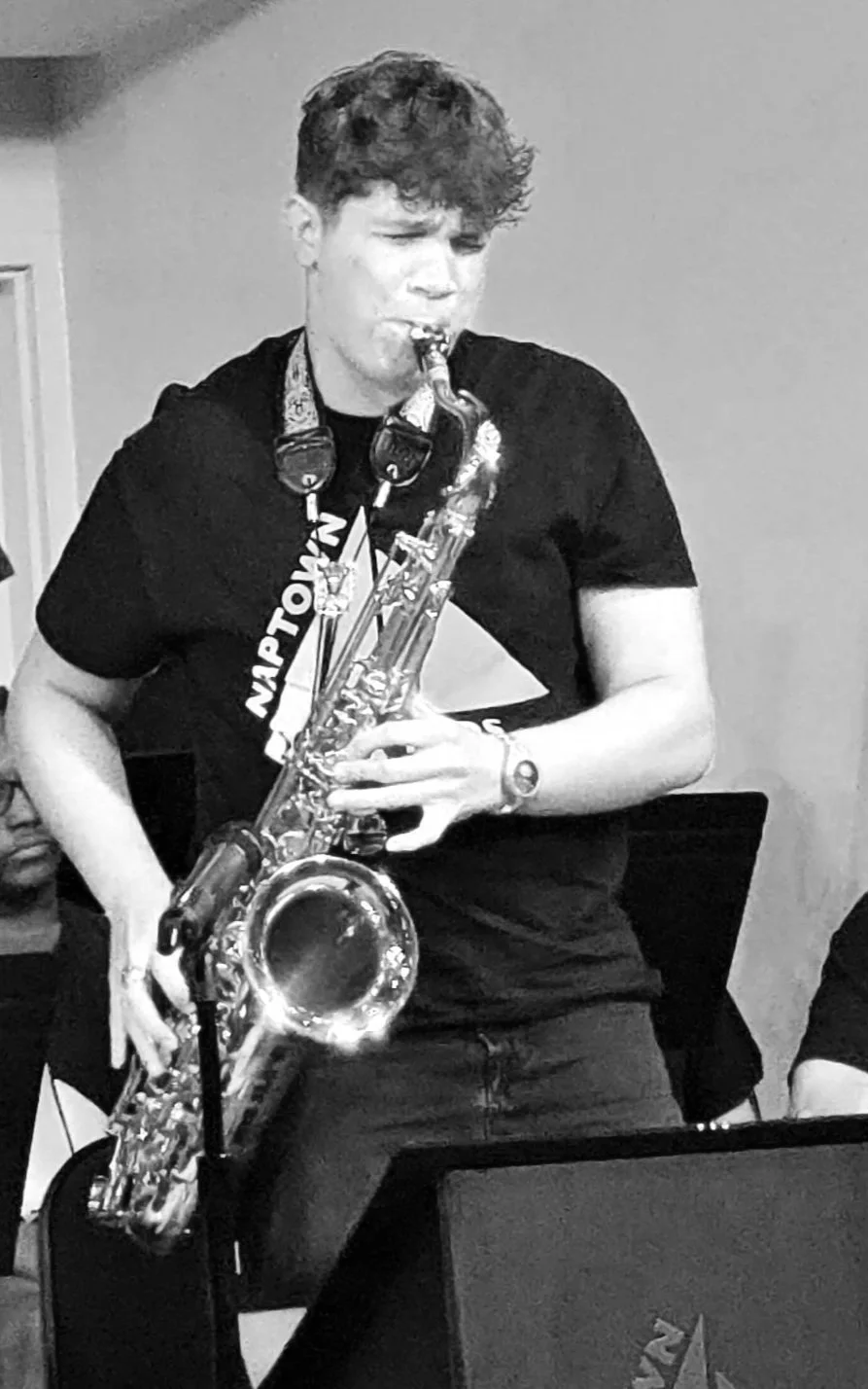 A young man with sailor-style headphones playing the saxophone during a music performance or rehearsal.