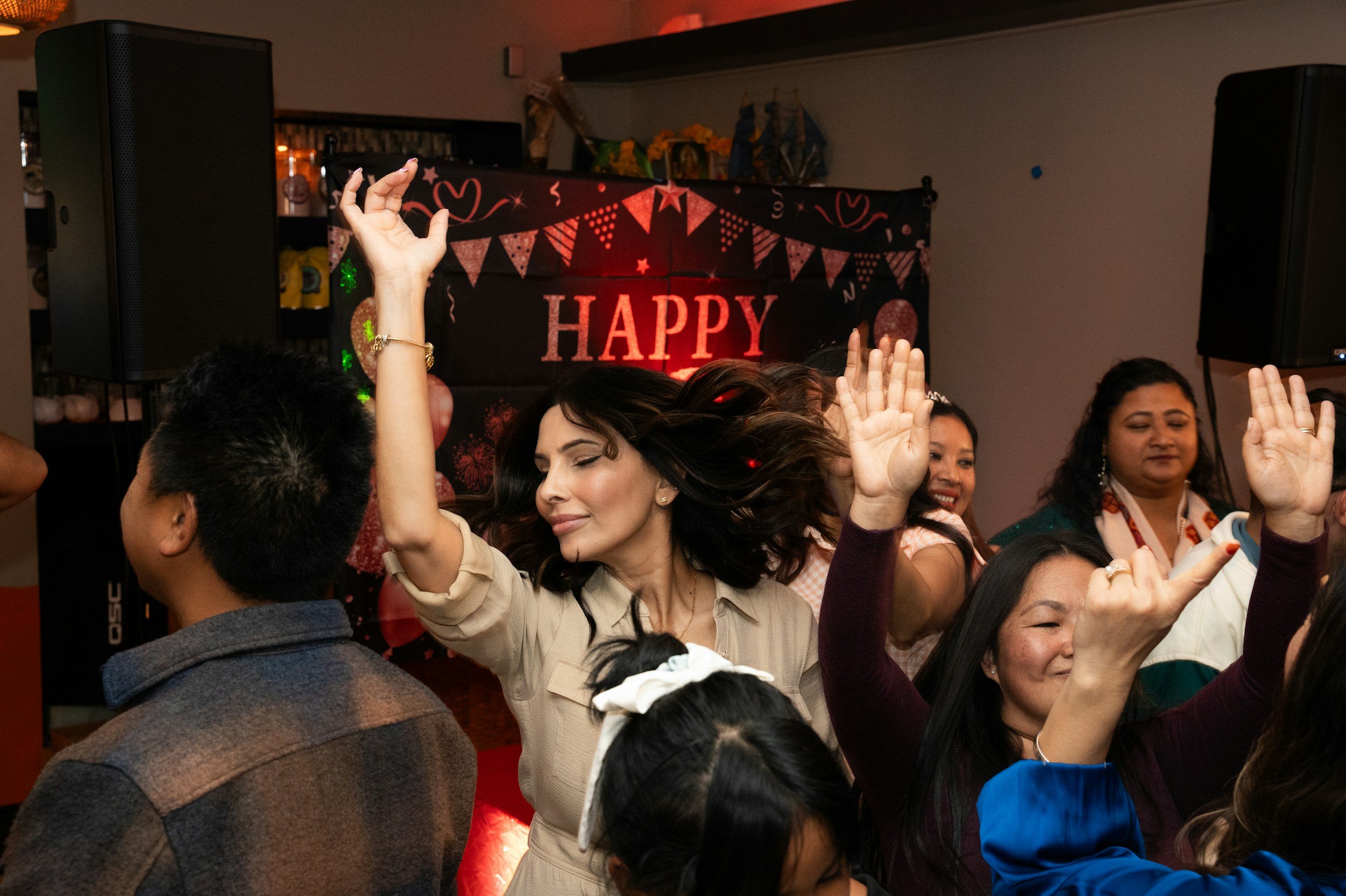 A group of people dancing at a celebration with a backdrop displaying the words 'HAPPY' and festive decorations.