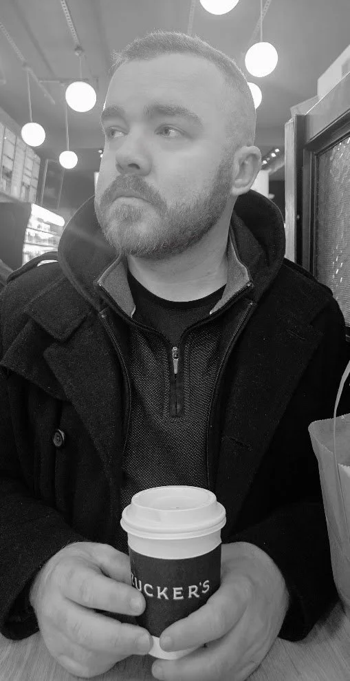 Man with beard holding a coffee cup in a cafe.
