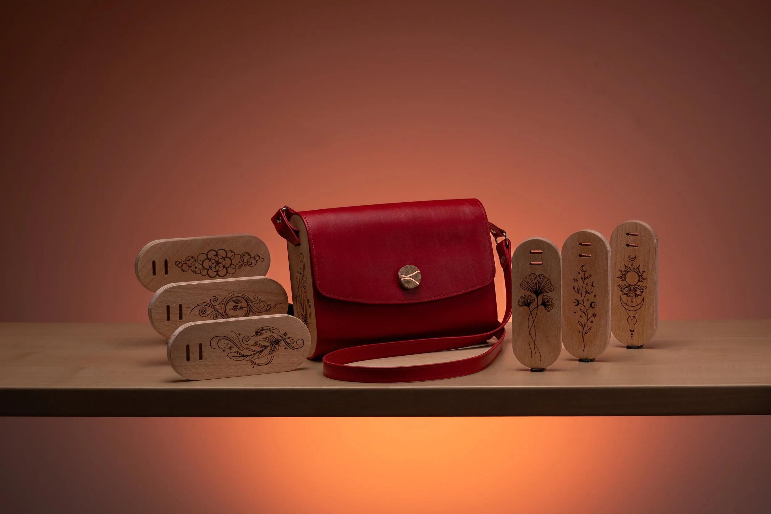 A row of six wooden massage tools with engraved designs, a red leather purse, and a set of four matching wooden massage tools with engraved designs, placed on a surface against a gradient background.
