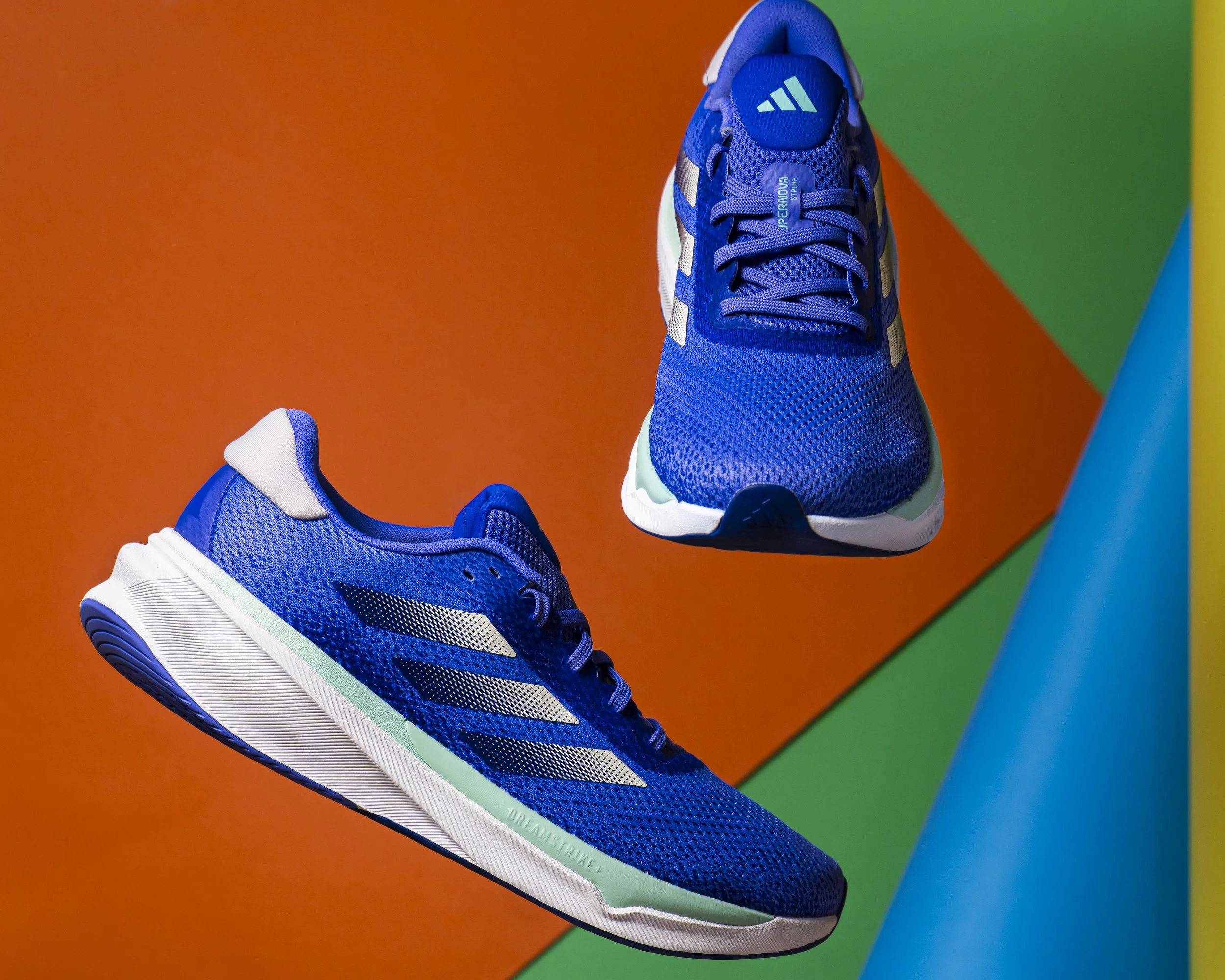 A blue athletic shoe with white and black accents, placed on an orange and green background.