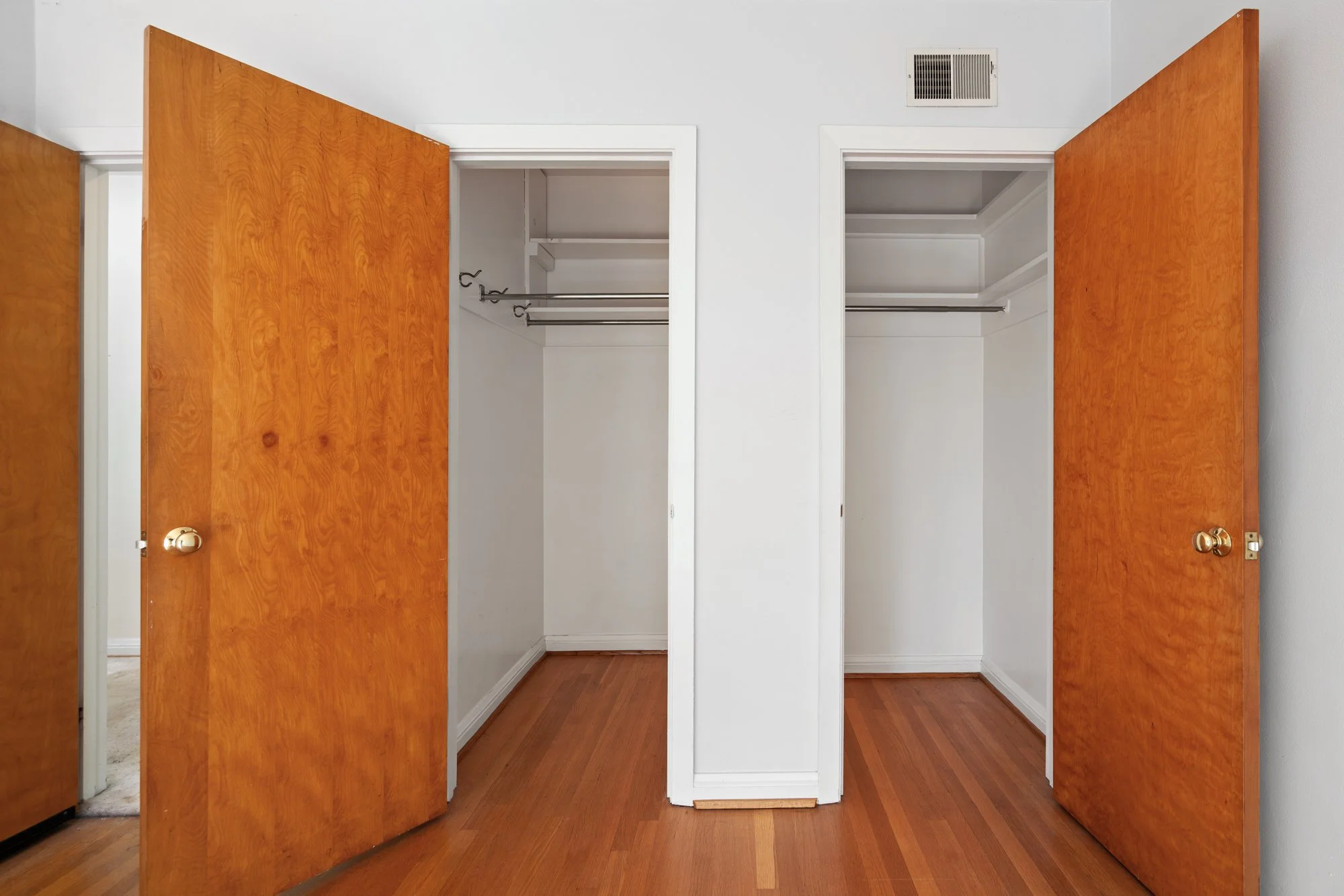 Two open closet doors with wooden finish show an empty closet with built-in shelves and hanging rods inside.