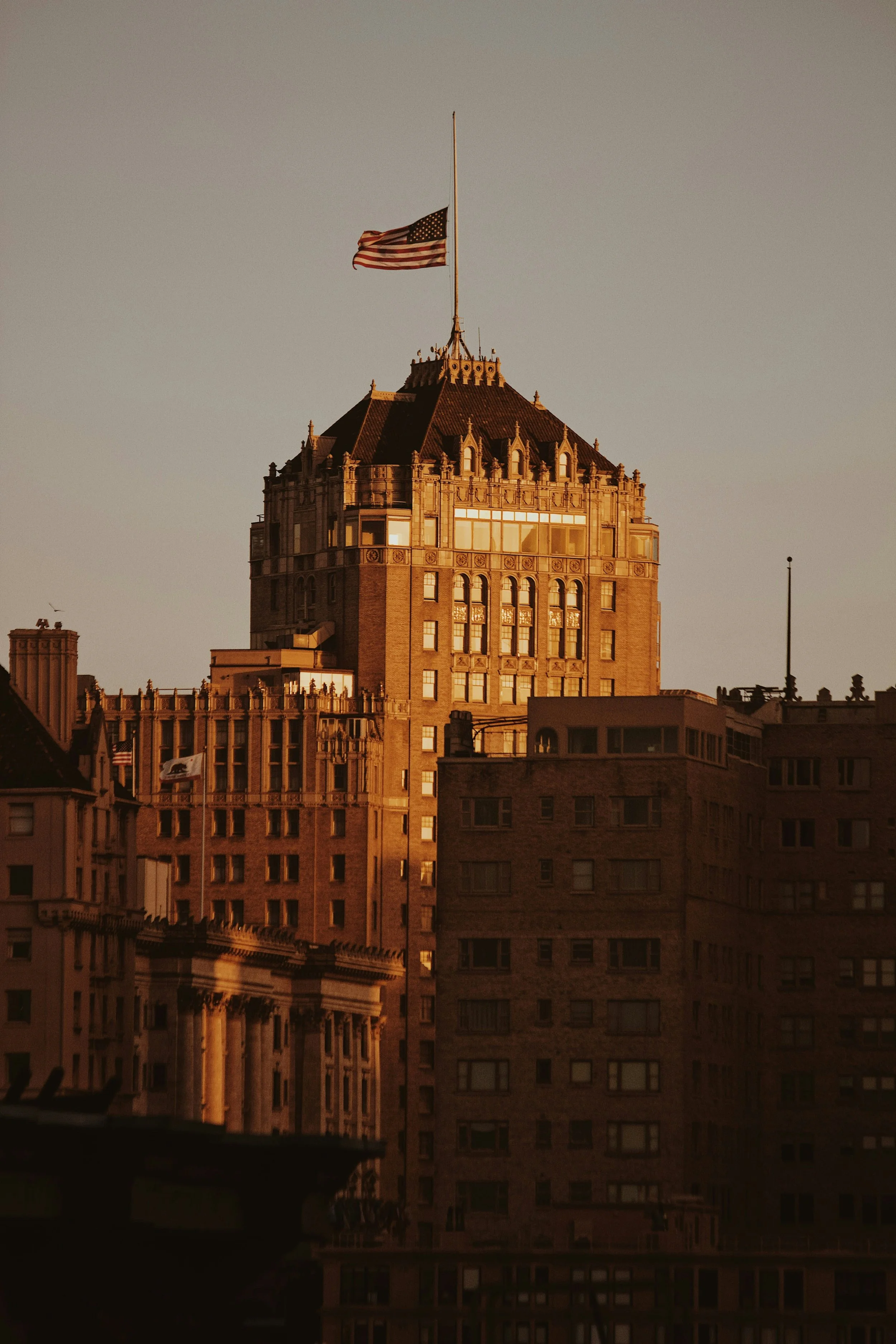 A tall building with ornate architecture at the top, featuring windows and decorative details, with an American flag flying on a flagpole at sunset.