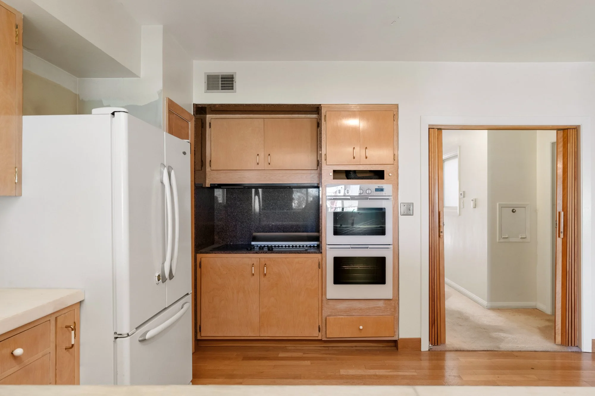 Kitchen with wooden cabinets, white appliances, black stove, and a doorway leading to a hallway.
