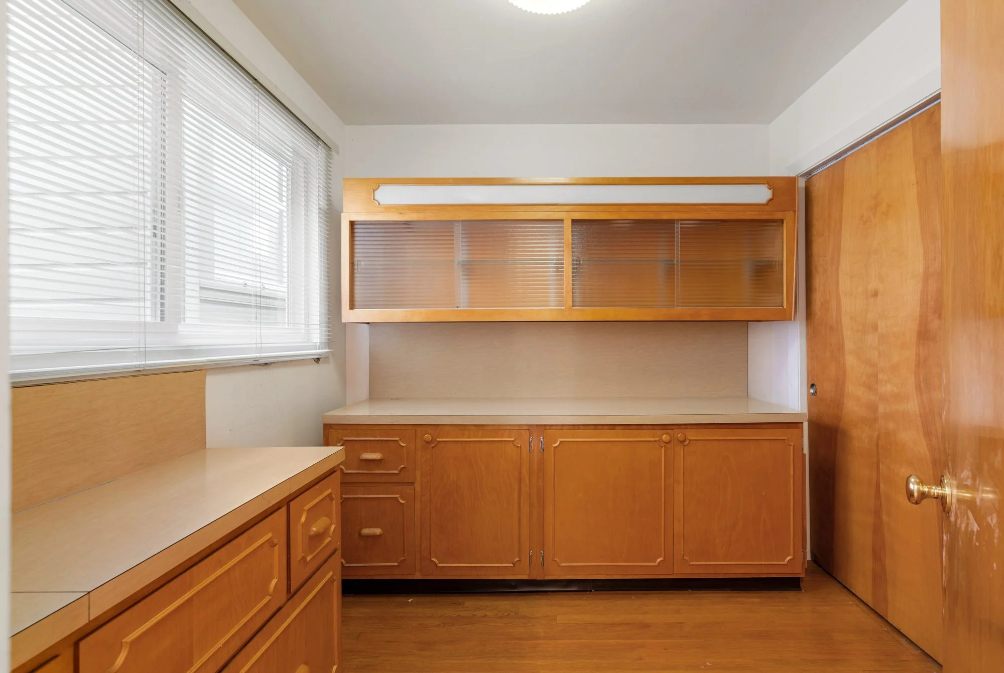 U-shaped kitchen with wooden cabinets, drawers, and a window with white blinds.