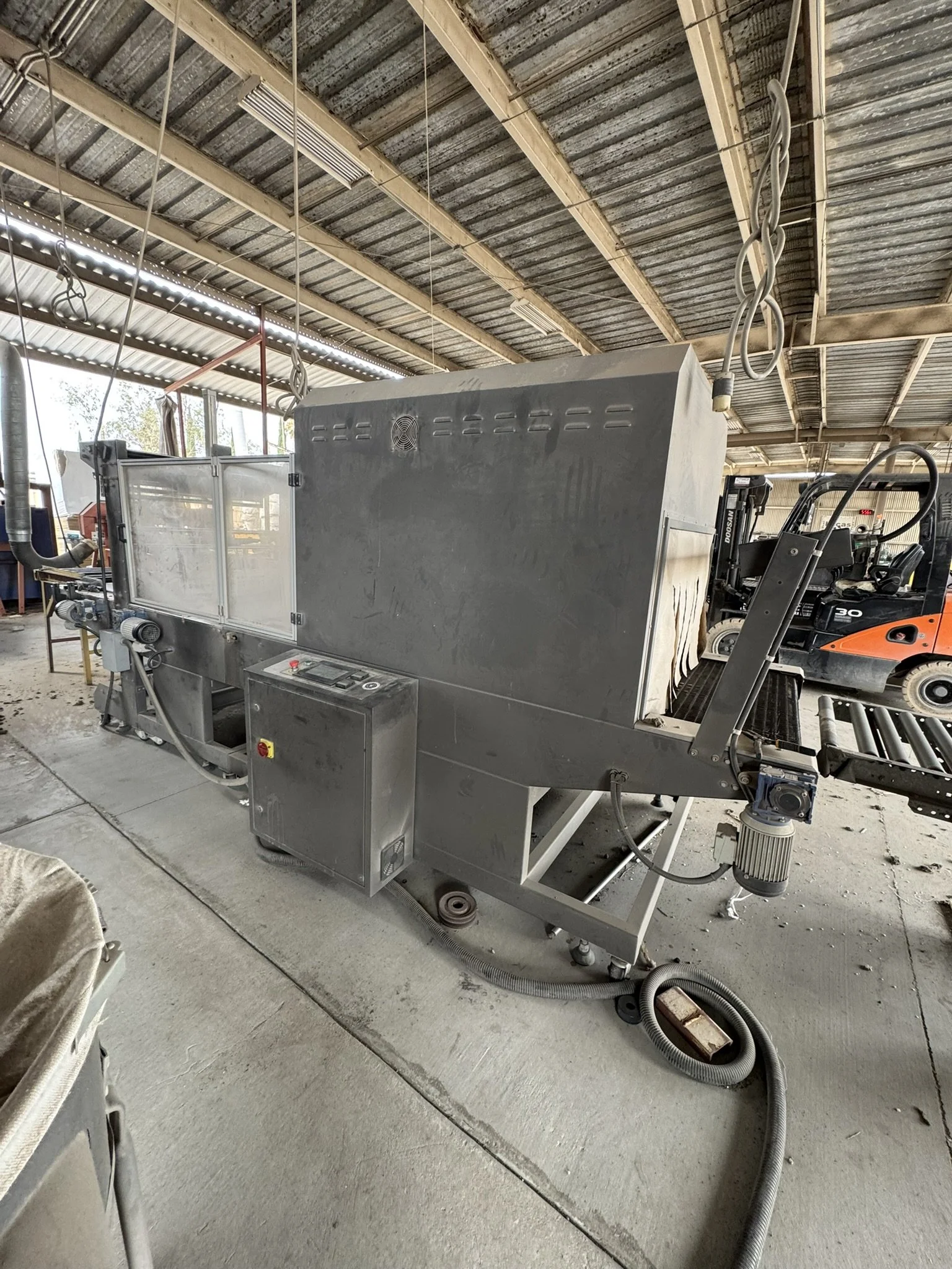 Industrial metal machine in a warehouse with forklifts and construction materials around.