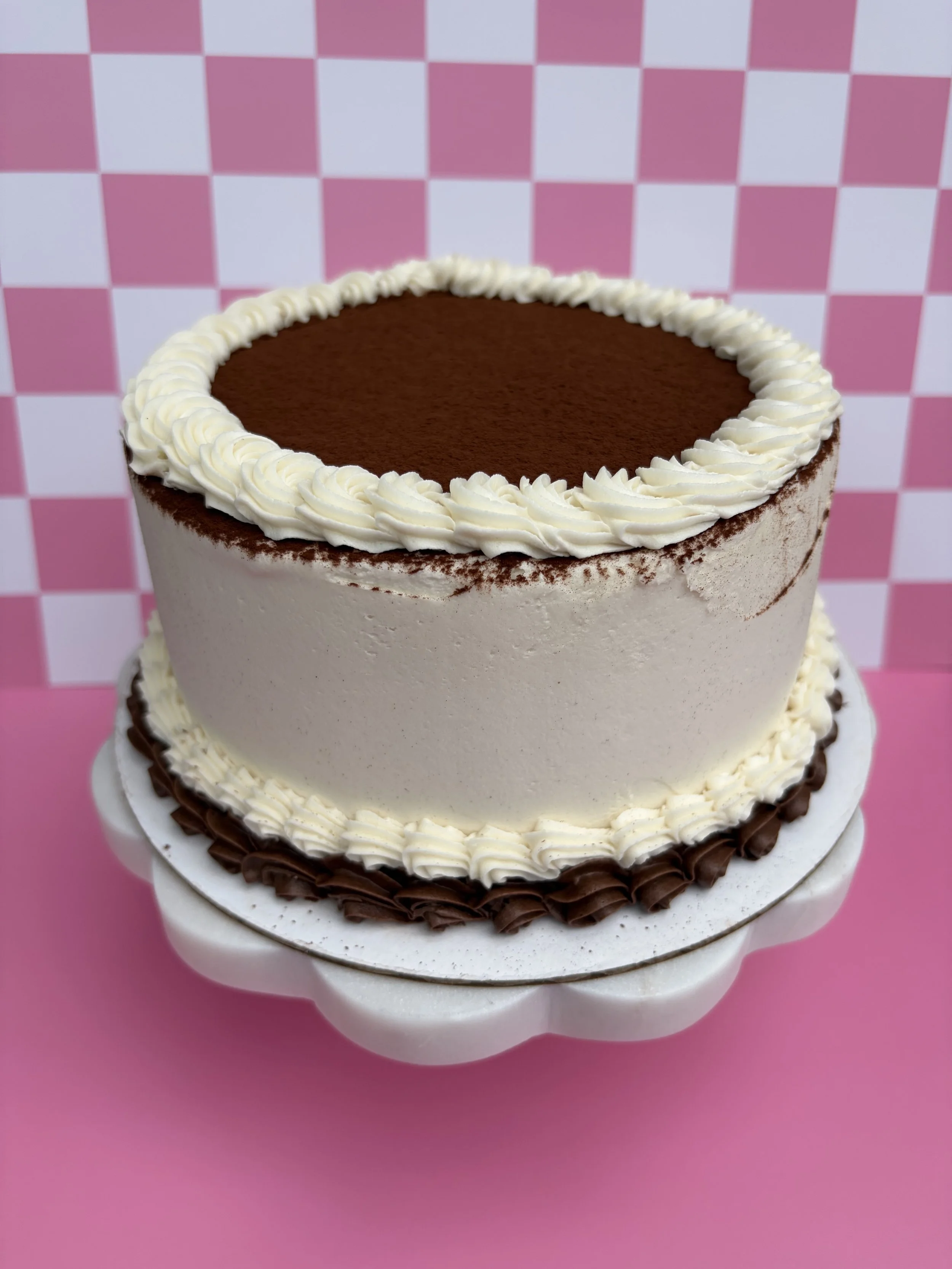 Two-tiered cake with white and chocolate frosting on a pink background.