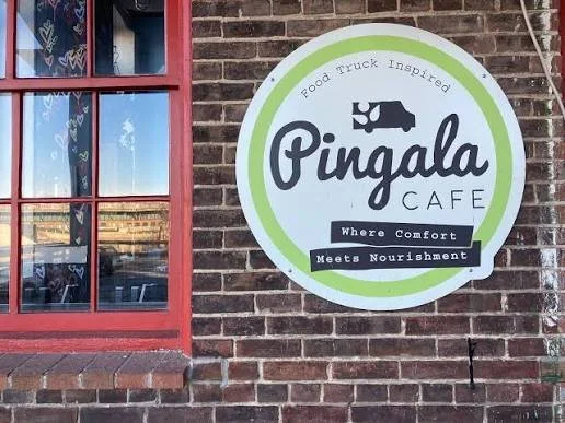 Sign for Pingala Cafe on a brick wall featuring a lion logo and the slogan 'Where Comfort Meets Nourishment'.